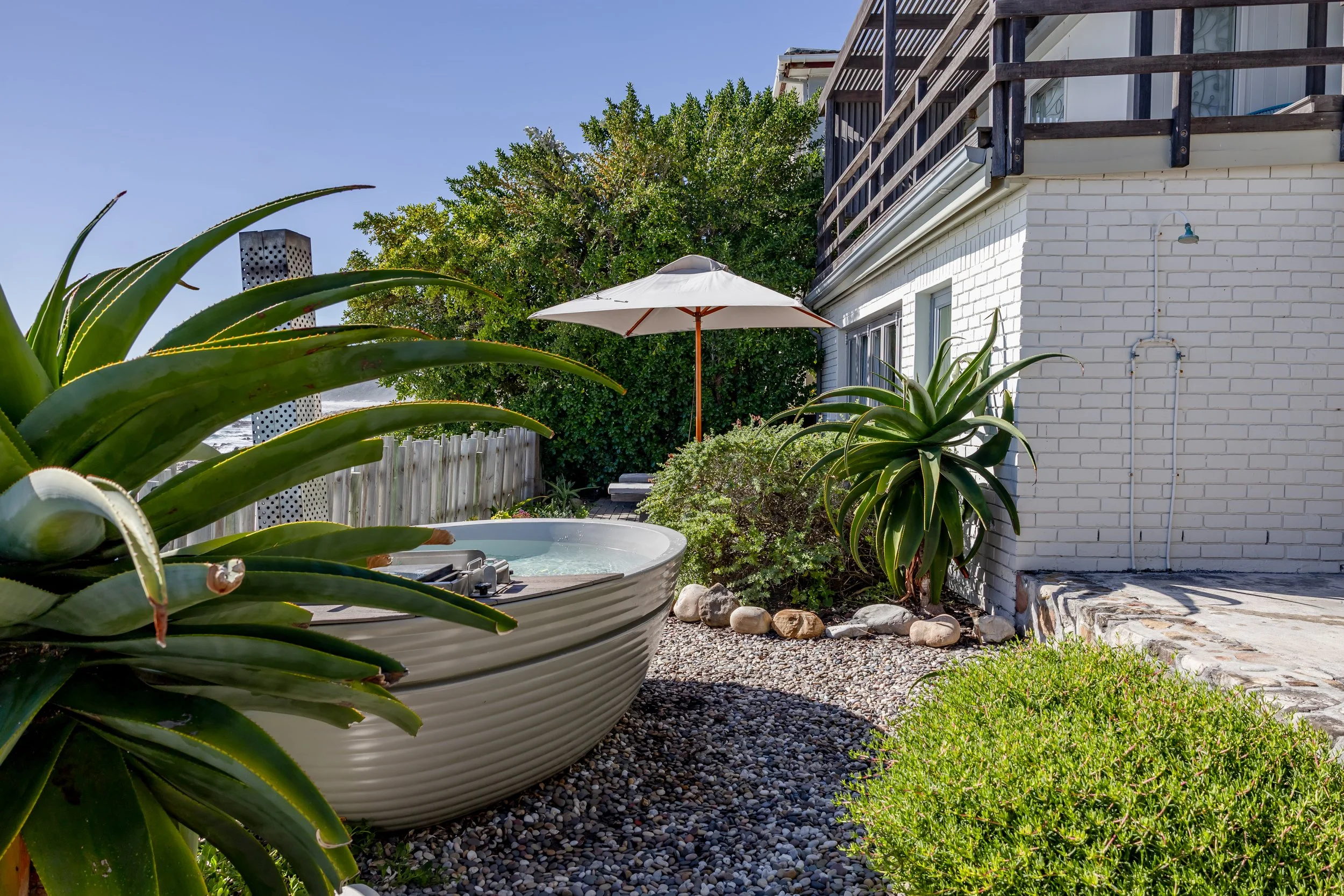 Lush green garden with a private hot tub, white patio umbrella, and coastal fynbos plants.