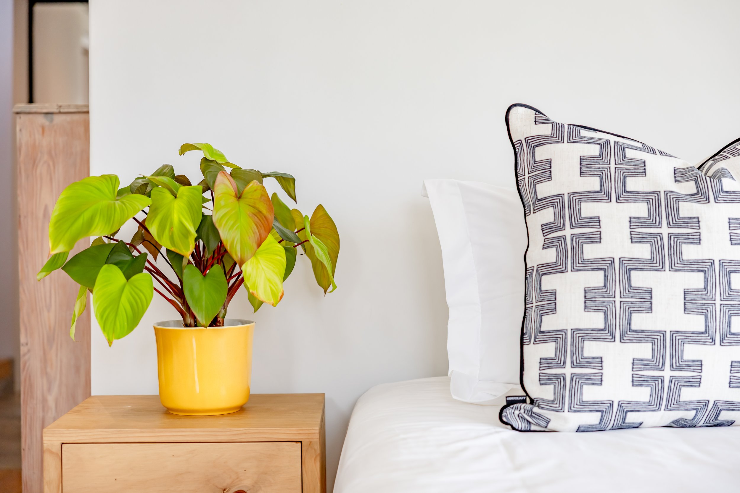 Detail shot of luxury Airbnb bedroom decor in Cape Town featuring a yellow bedside lamp and patterned accent pillows.