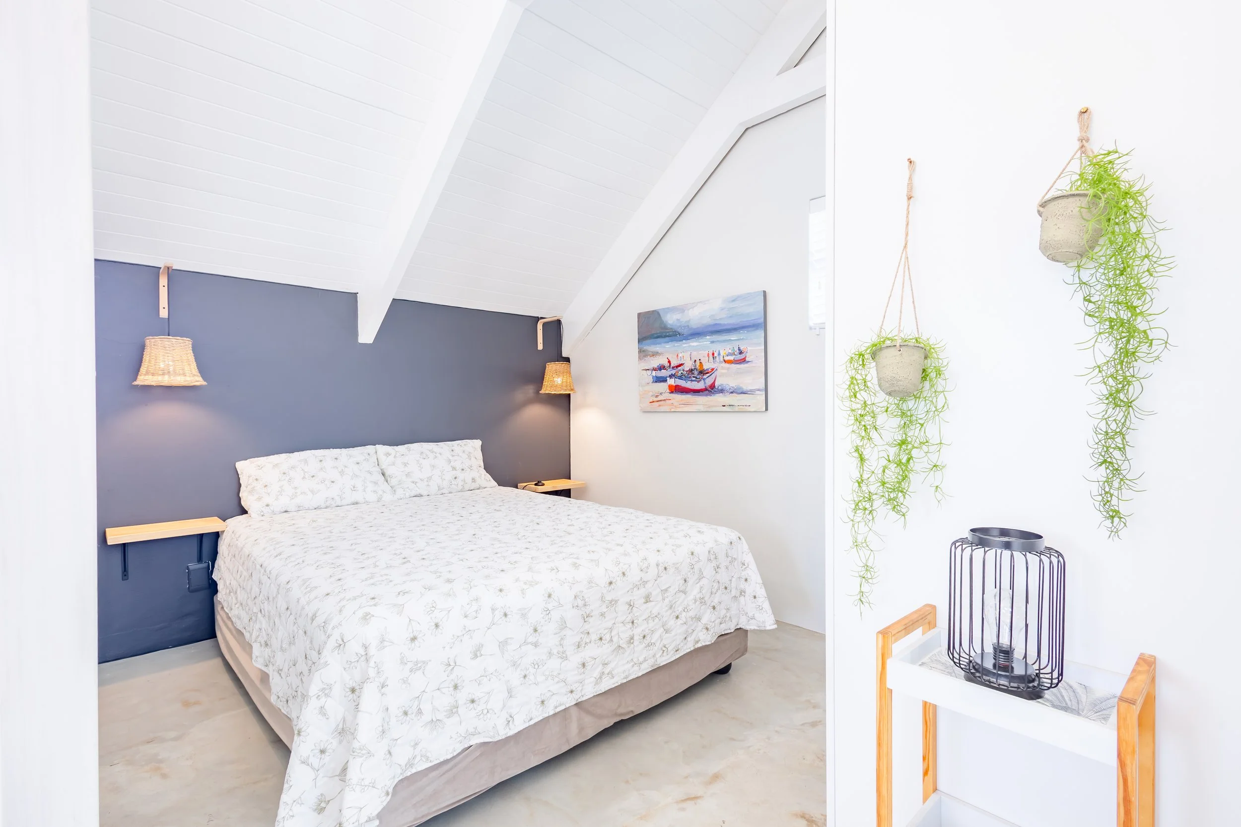 Minimalist bedroom photography for a luxury coastal escape, highlighting crisp white linens, a navy accent wall, and natural light from large windows.