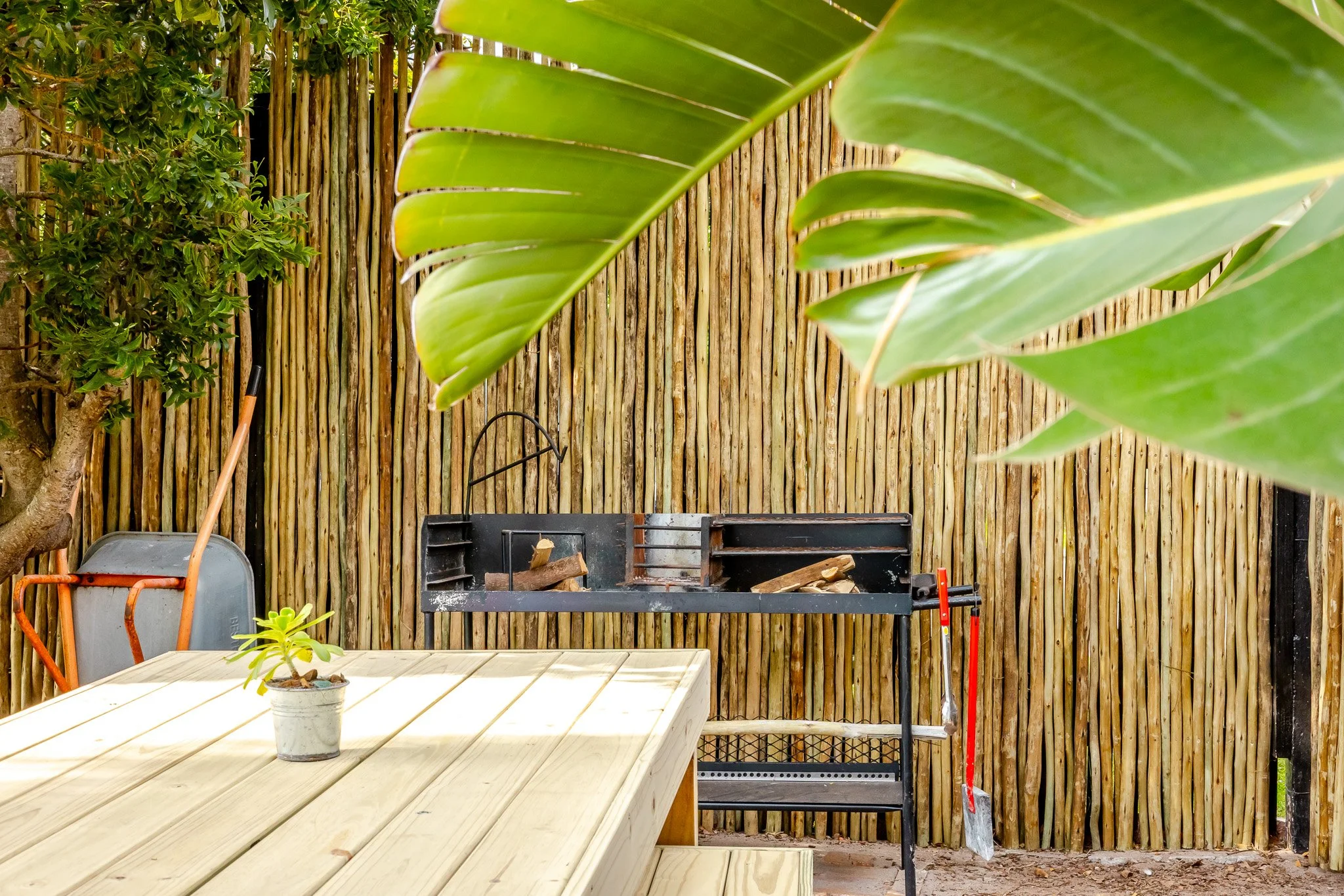 Lifestyle photography of a traditional South African braai area in a Kommetjie garden, featuring wooden decking and bamboo fencing.