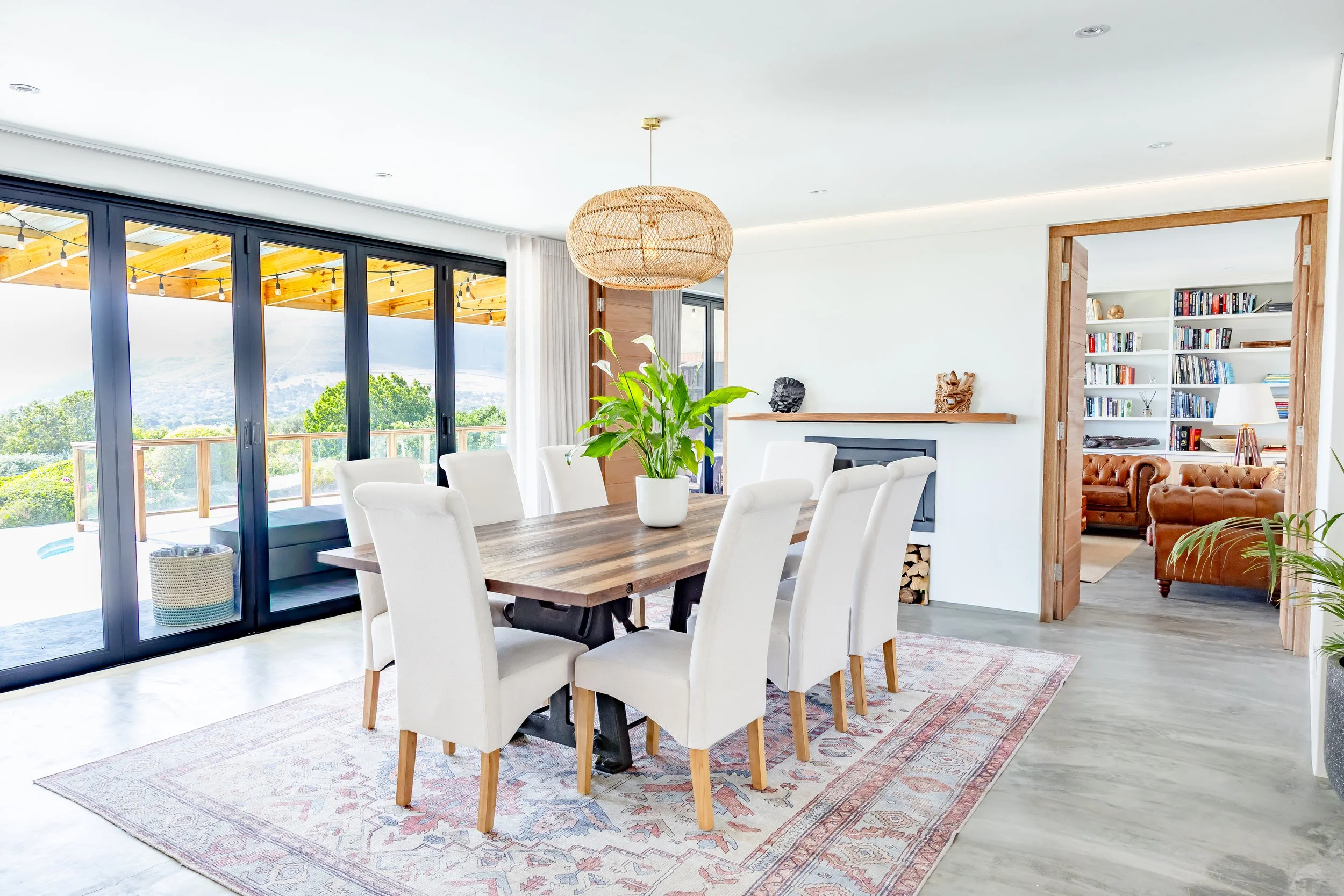 Sophisticated dining room interior in a Constantia villa featuring a large wooden table, white upholstered chairs, and an ornate rug.