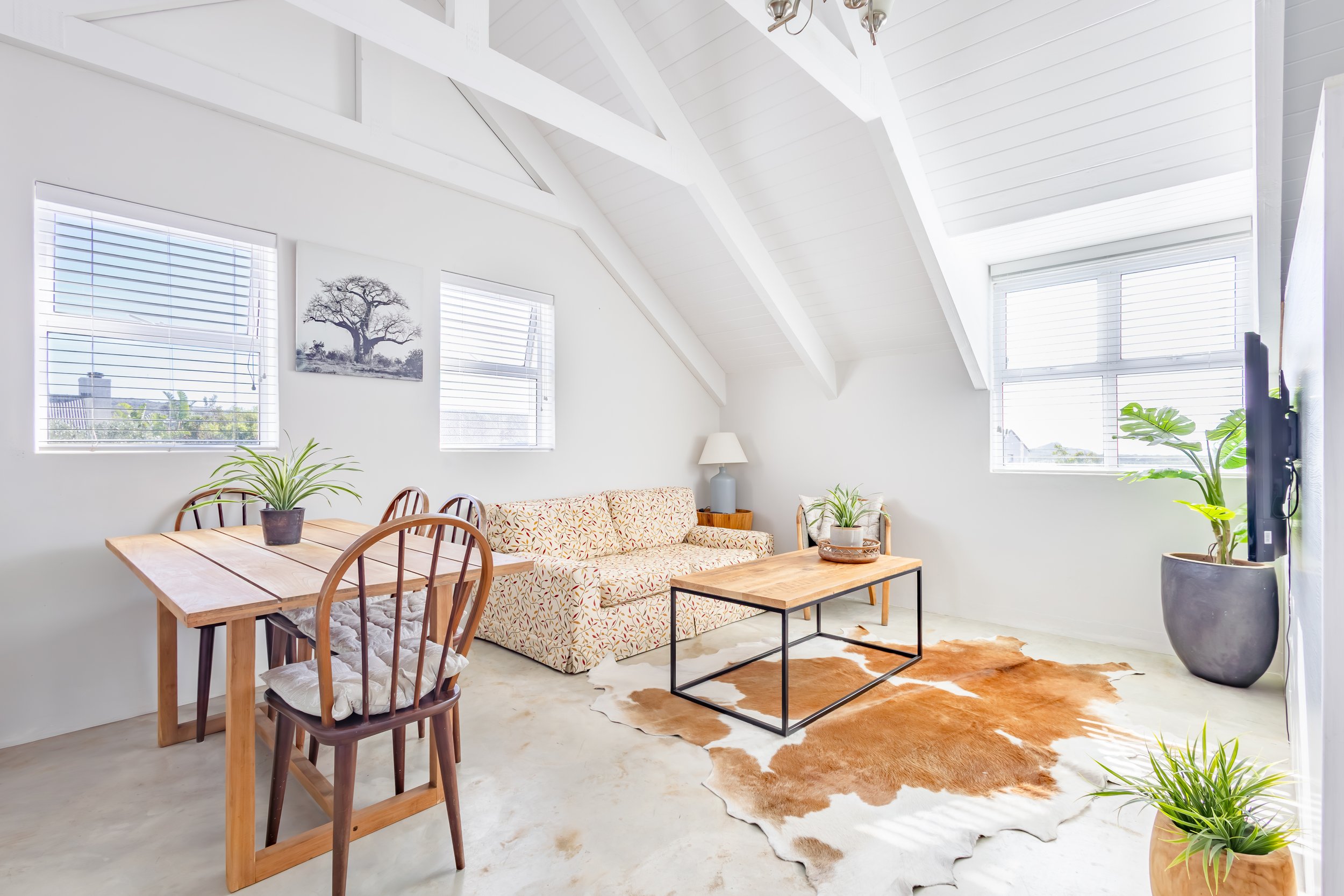 Bright and airy studio apartment interior in Cape Town featuring a minimalist lounge area with a cowhide rug, wooden coffee table, and vaulted ceilings, professionally photographed for Airbnb.