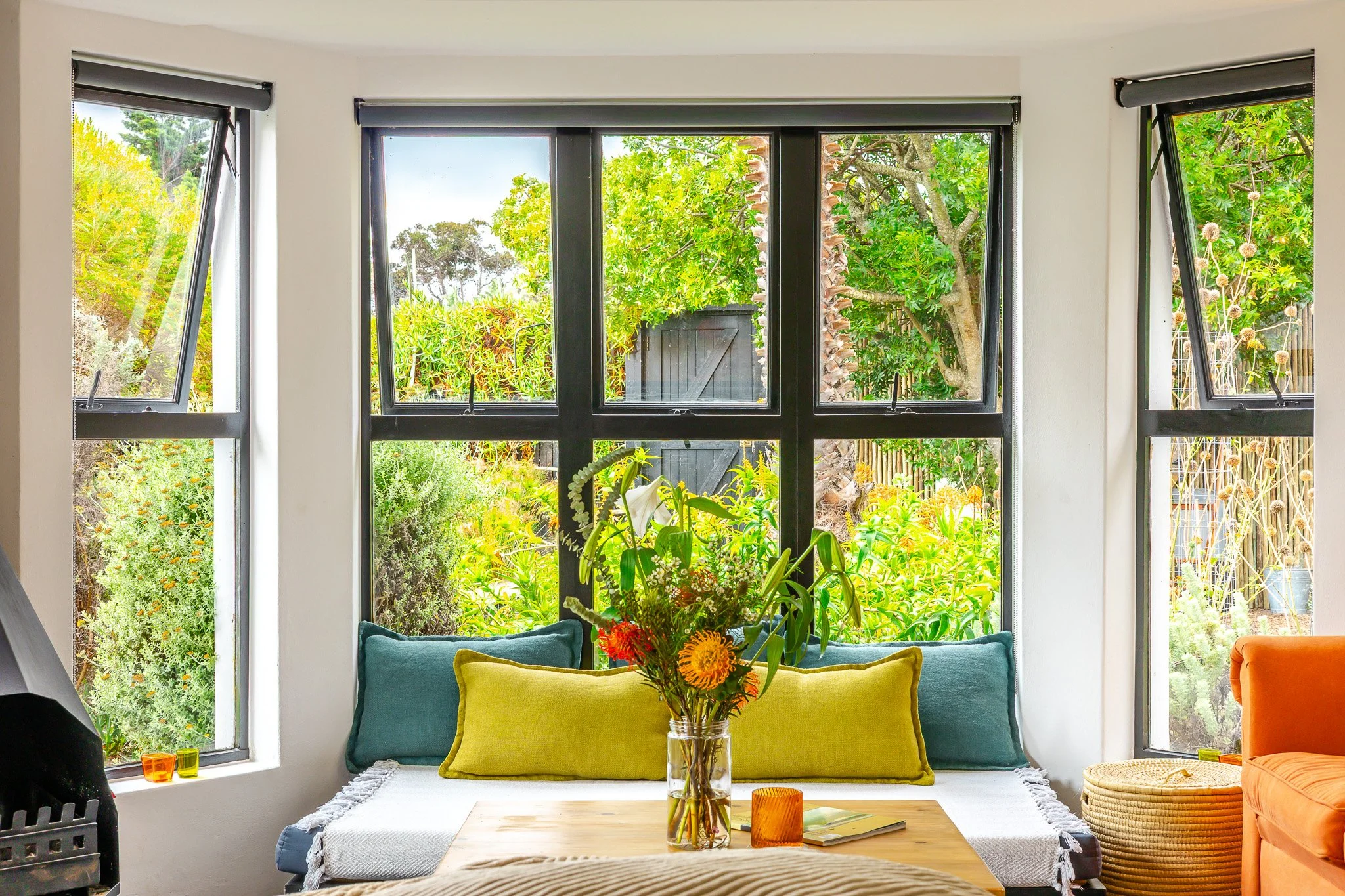 Interior detail shot of a bright window seat in a Cape Town coastal home, highlighting vibrant yellow cushions and natural garden views.