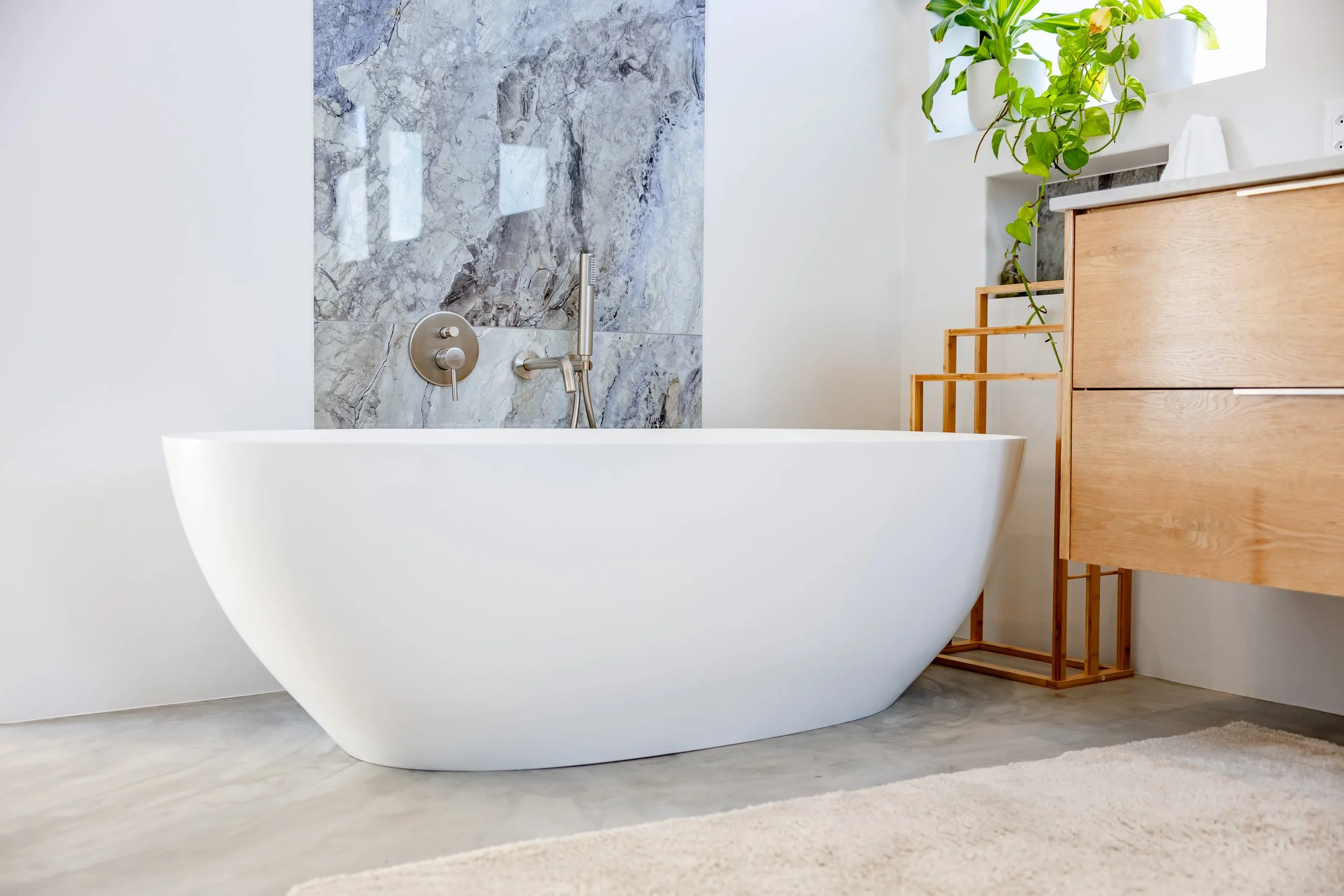 Luxury bathroom photography in Clifton showcasing a modern freestanding white bathtub against a marble feature wall.