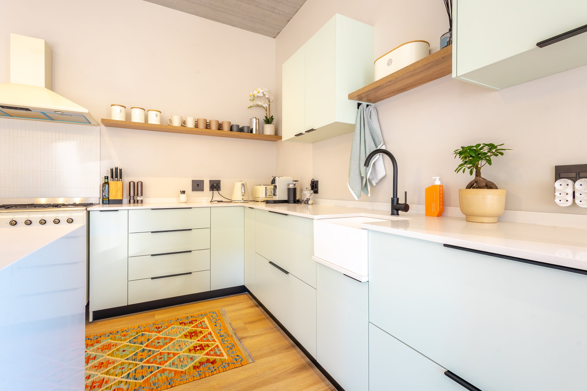 Modern kitchen with white countertops, mint green cabinets, black hardware, a black faucet, and a decorative pot with a bonsai tree on the counter.