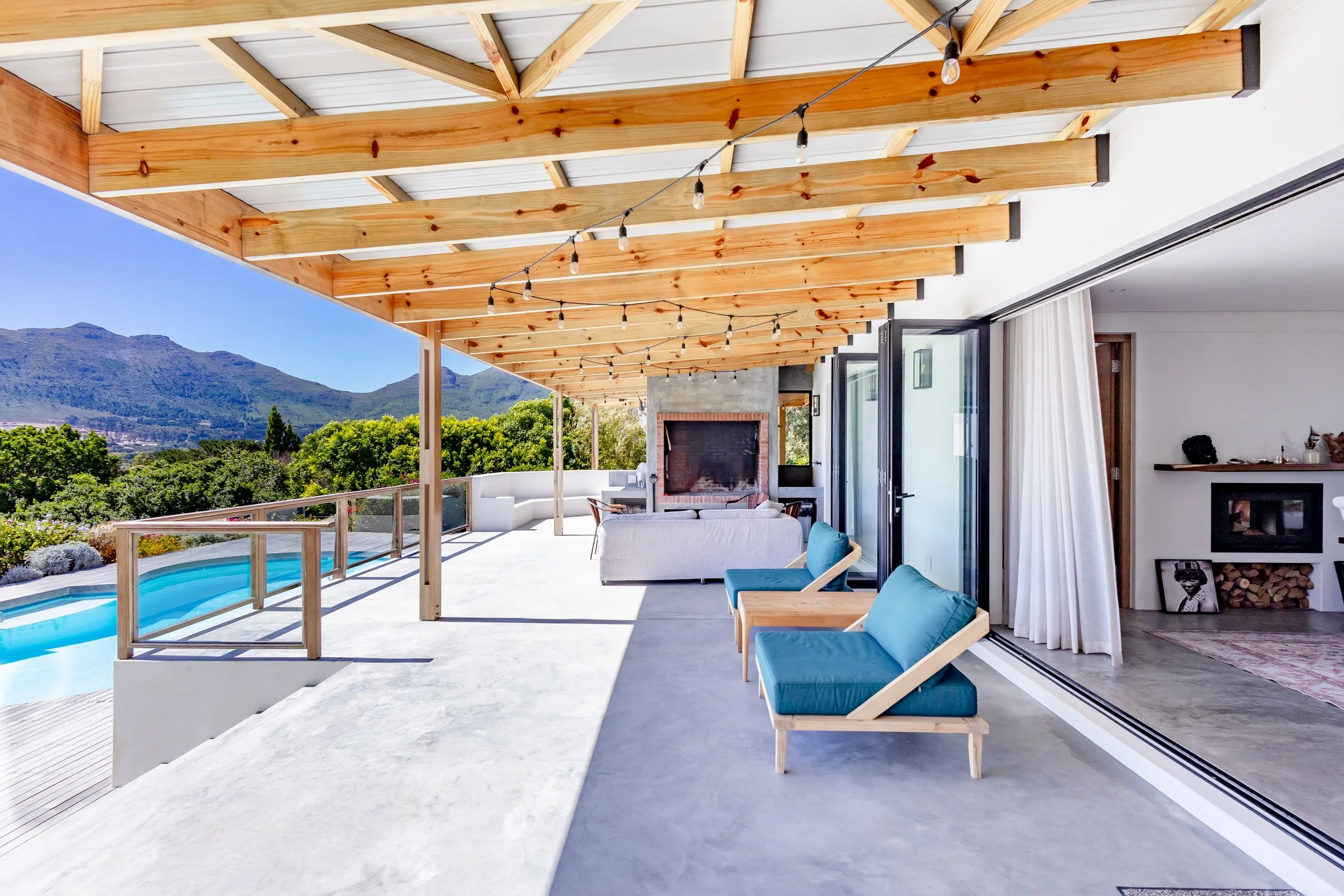 Atlantic Seaboard outdoor entertainment deck with teal designer loungers under a rustic wooden pergola.