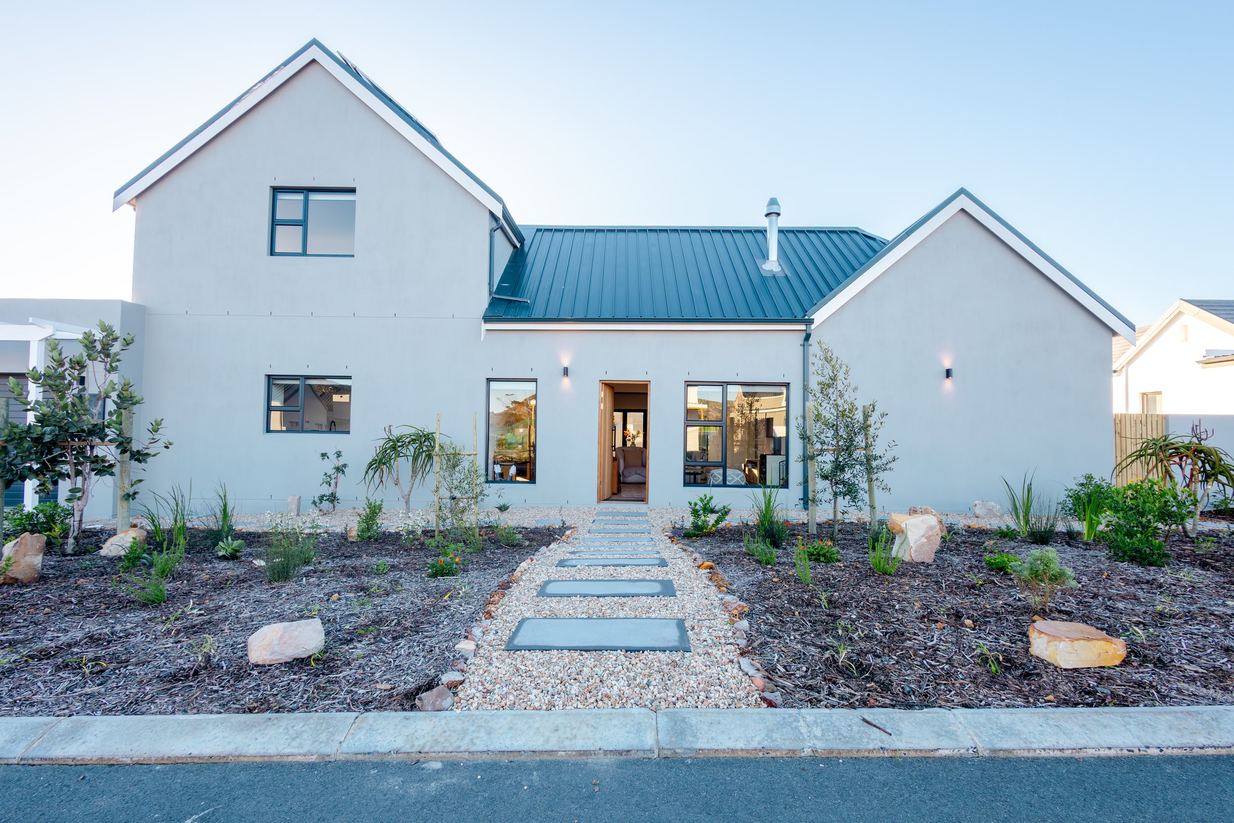 Modern two-story house with a gravel pathway leading to the front door and a landscaped yard with small trees and plants.