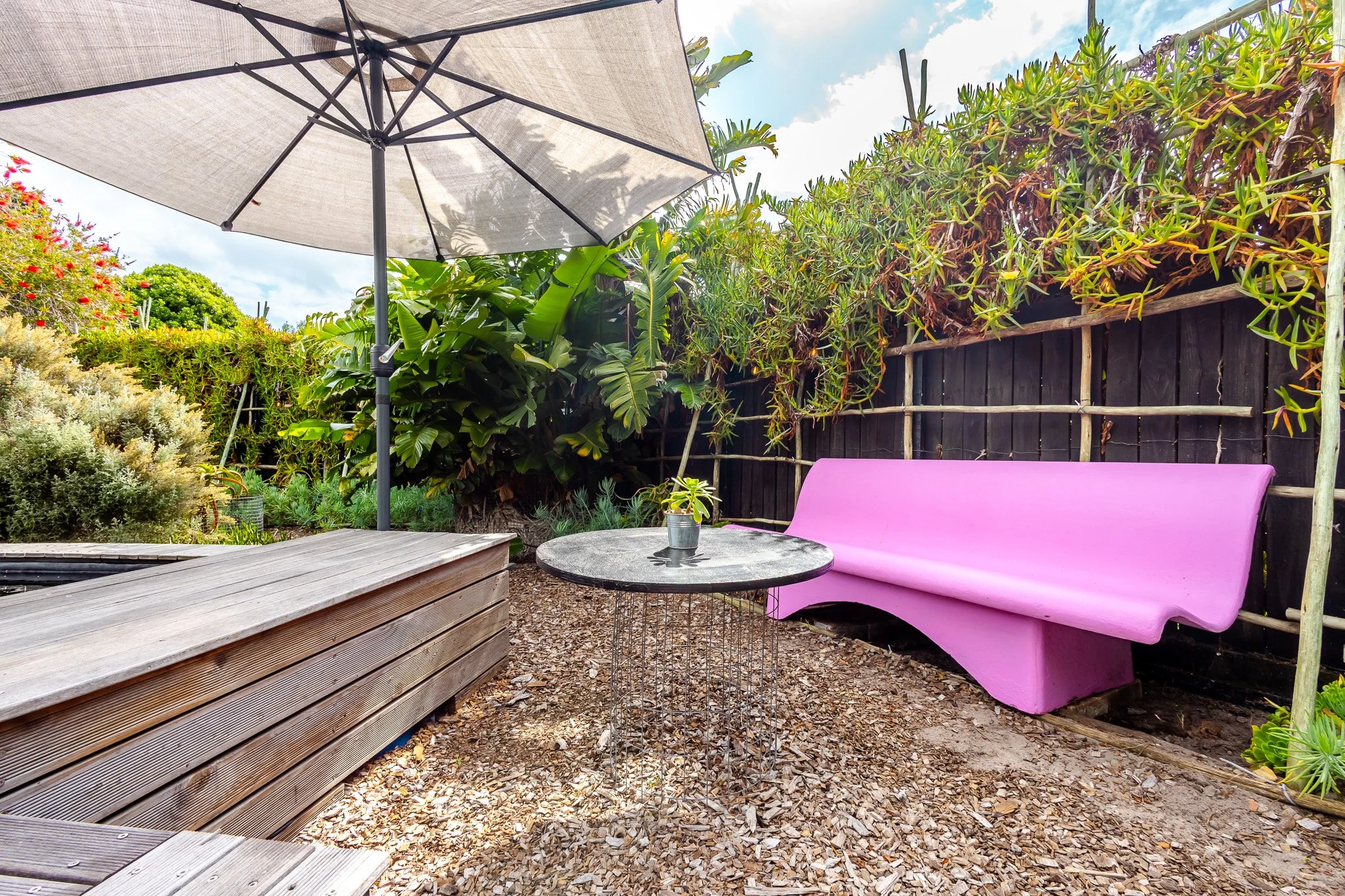High-end outdoor entertainment space in Cape Town featuring a bright pink designer bench, gravel patio, and large sun umbrella.