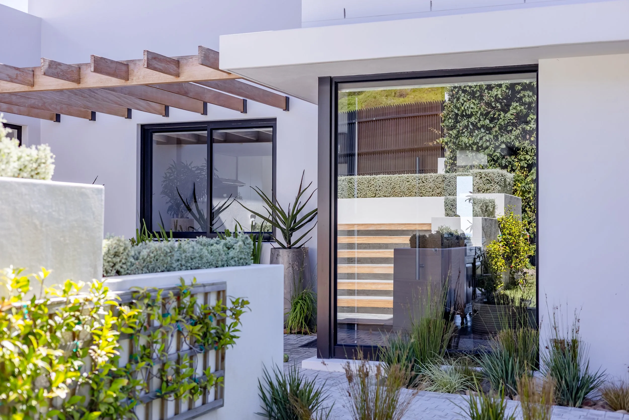 Exterior architectural detail of a luxury villa entrance in Constantia Upper featuring modern landscaping and a wooden pergola.