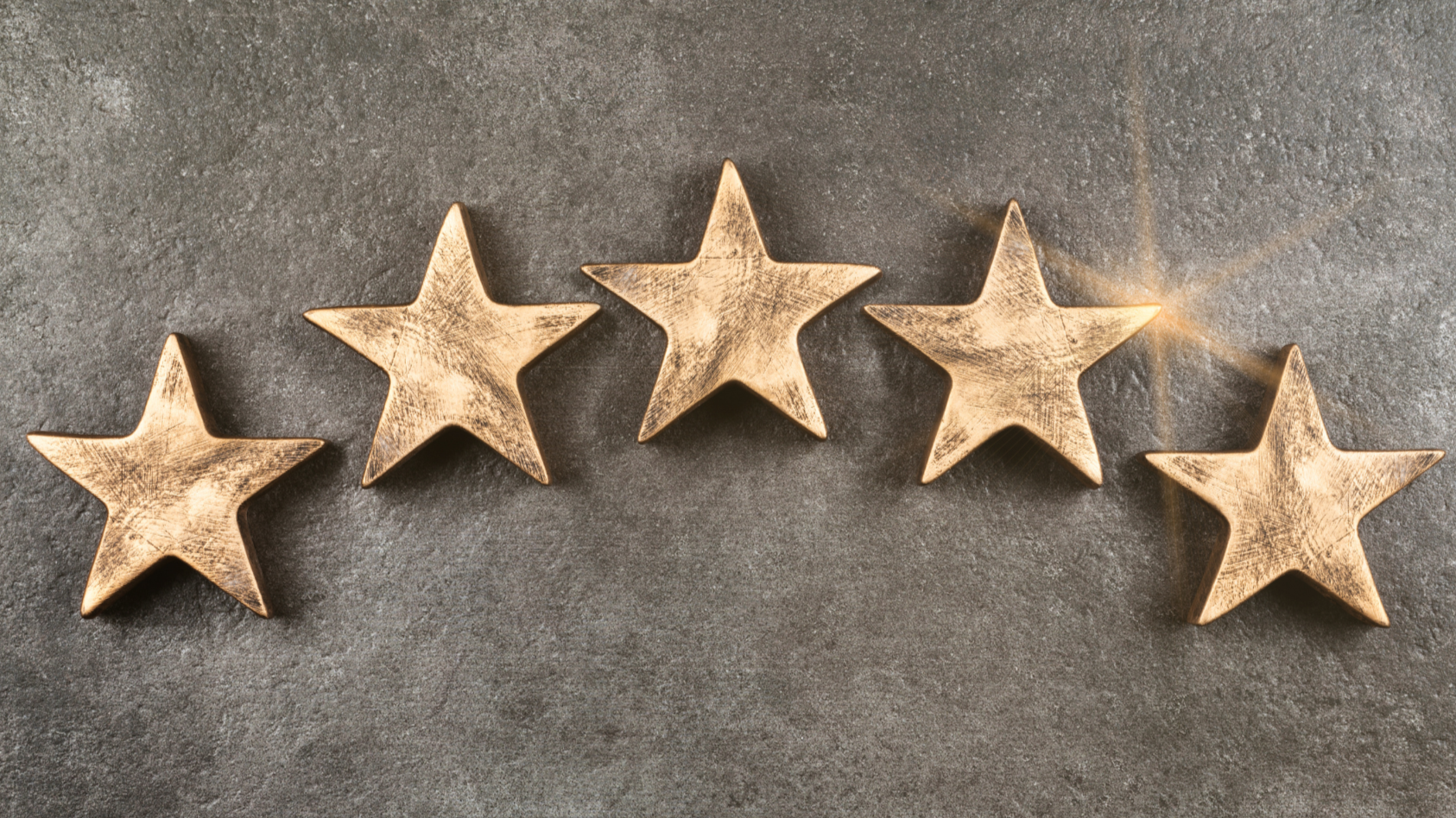 Five gold-colored five-pointed stars arranged in a curved line on a gray textured surface, with a star emitting light in the upper right.
