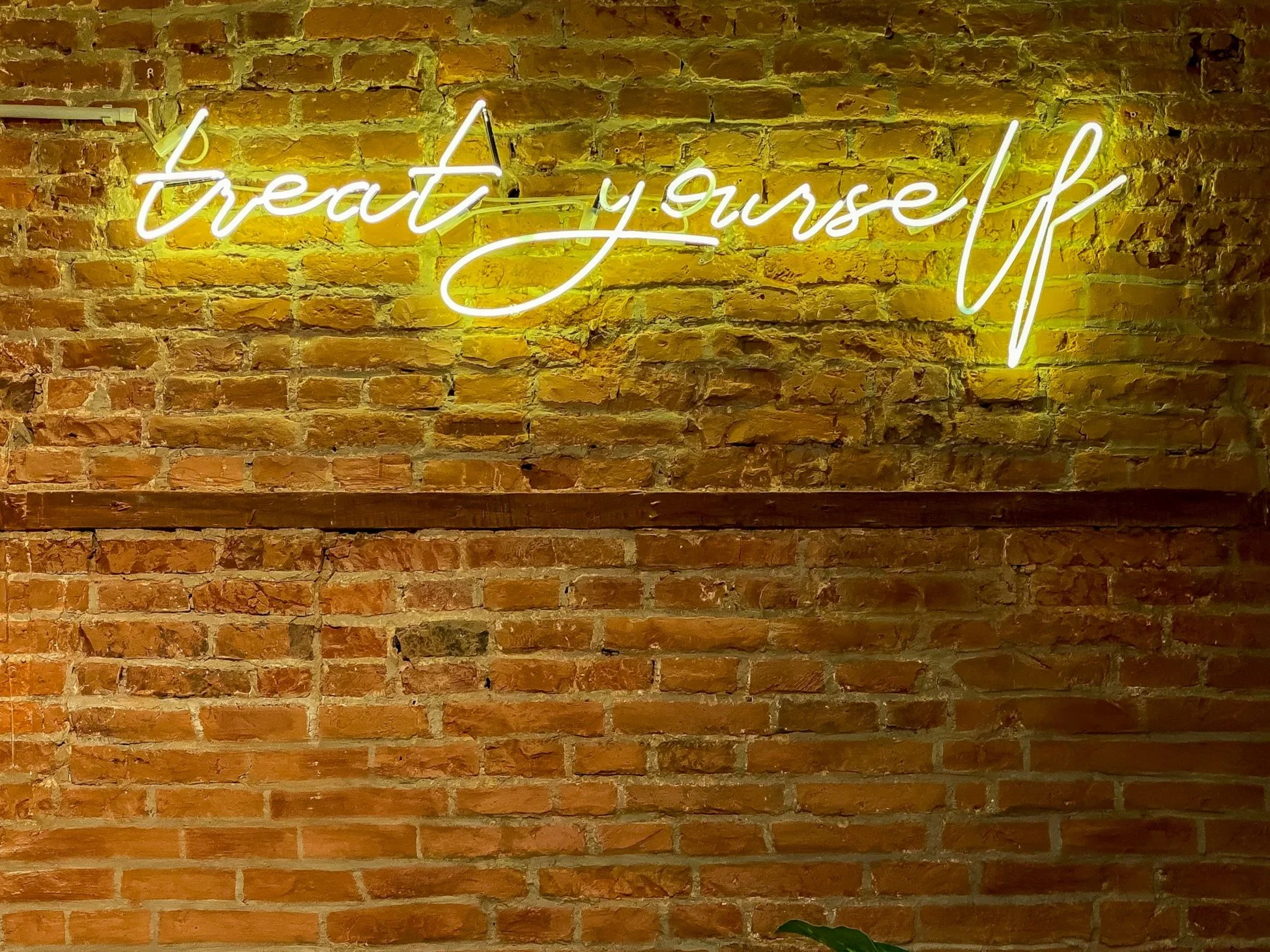 Neon sign on brick wall that reads "treat yourself" in cursive yellow and white lettering.