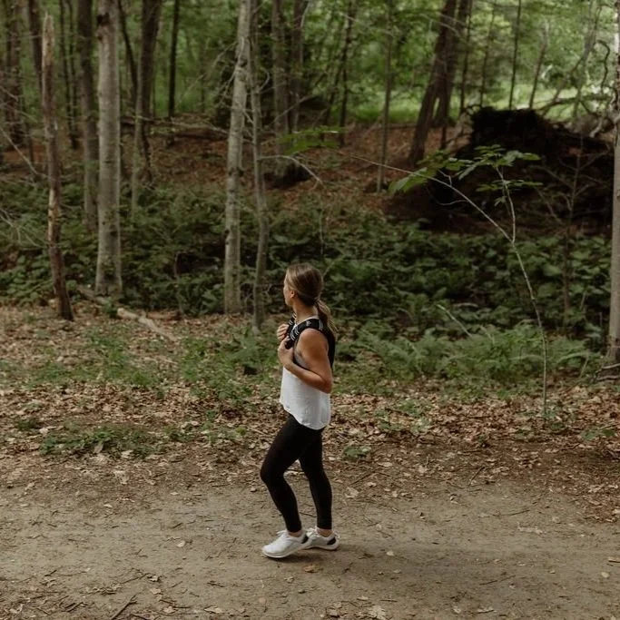 A woman jogging on a dirt trail through a forested area.