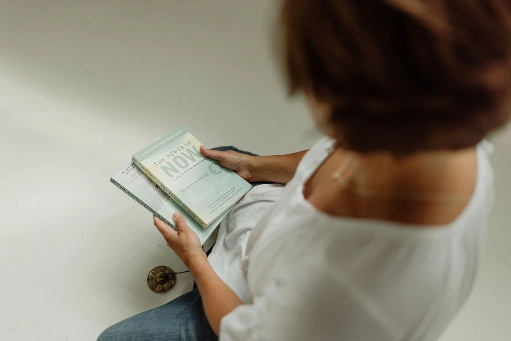 A woman sitting on the floor reading a book titled 'The Power of Now' by Eckhart Tolle.