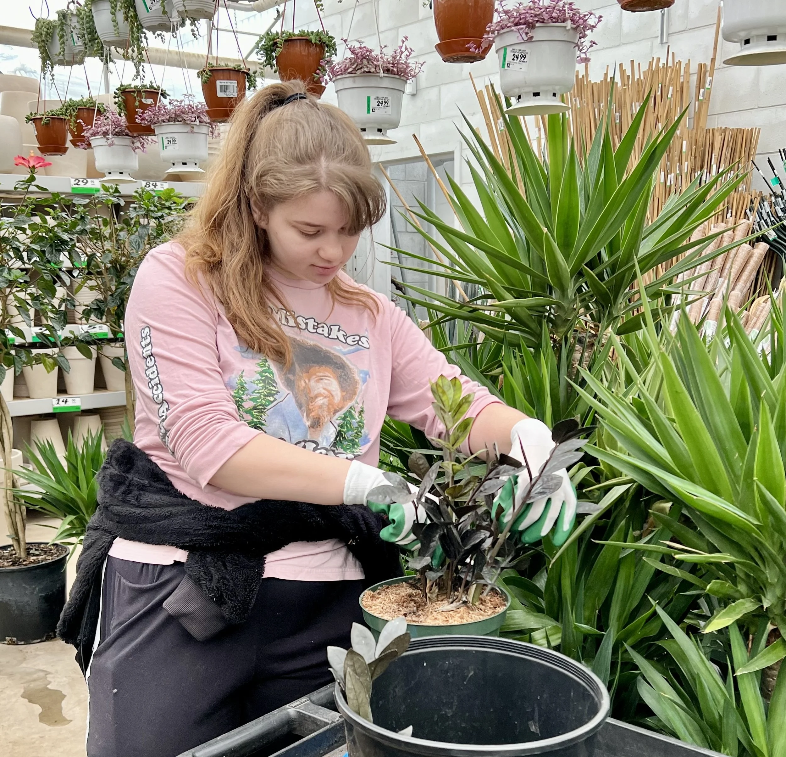 Une jeune femme en gants vert et blanc plante de jeunes pousses dans un pot de fleurs dans une jardinerie.