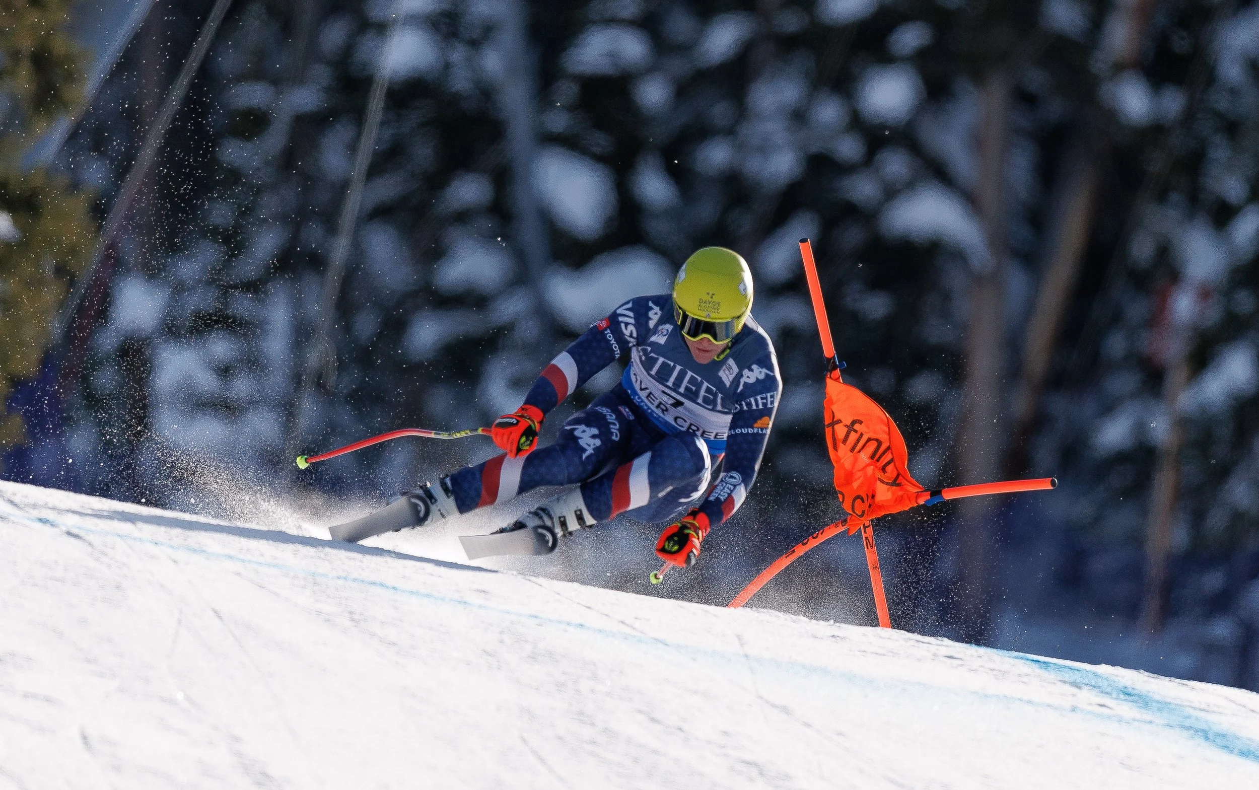 Alpine ski racer in a yellow helmet turning past a red race gate