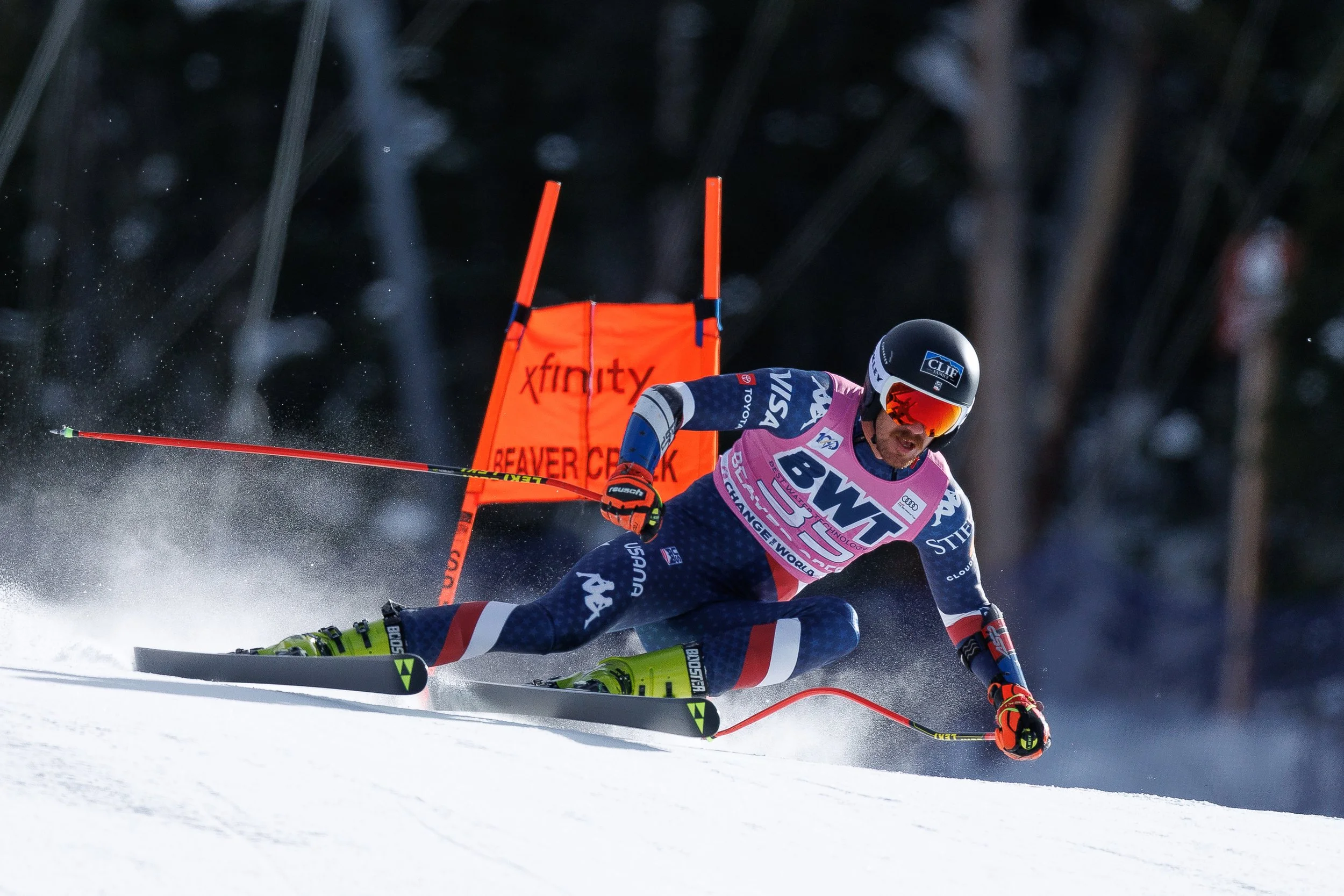 Alpine ski racer carving a turn beside a red race gate on a snowy course