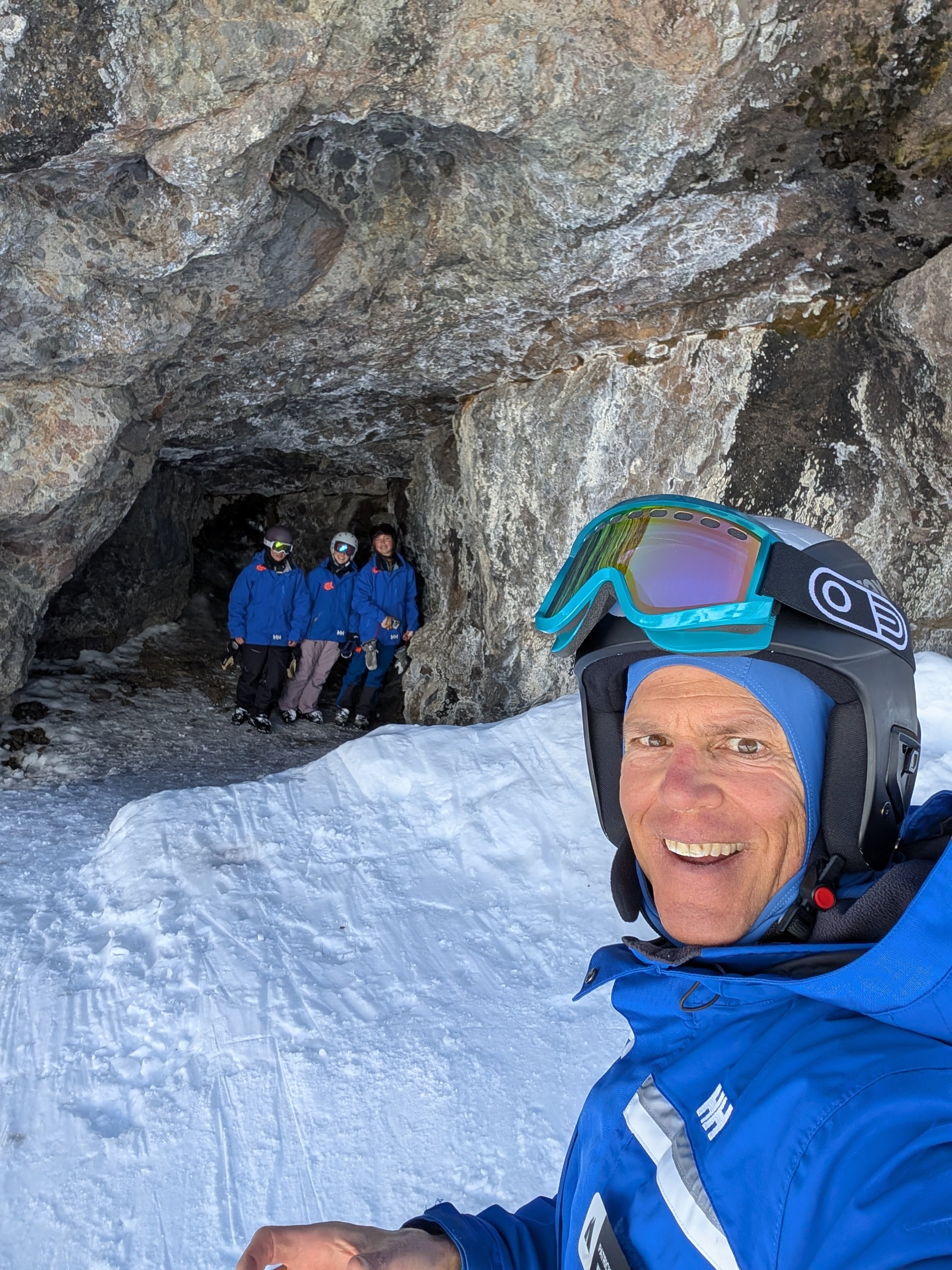 Patrick Traynor, KSEF U10 head coach, smiling in ski gear with young skiers beside a snowy rock formation.