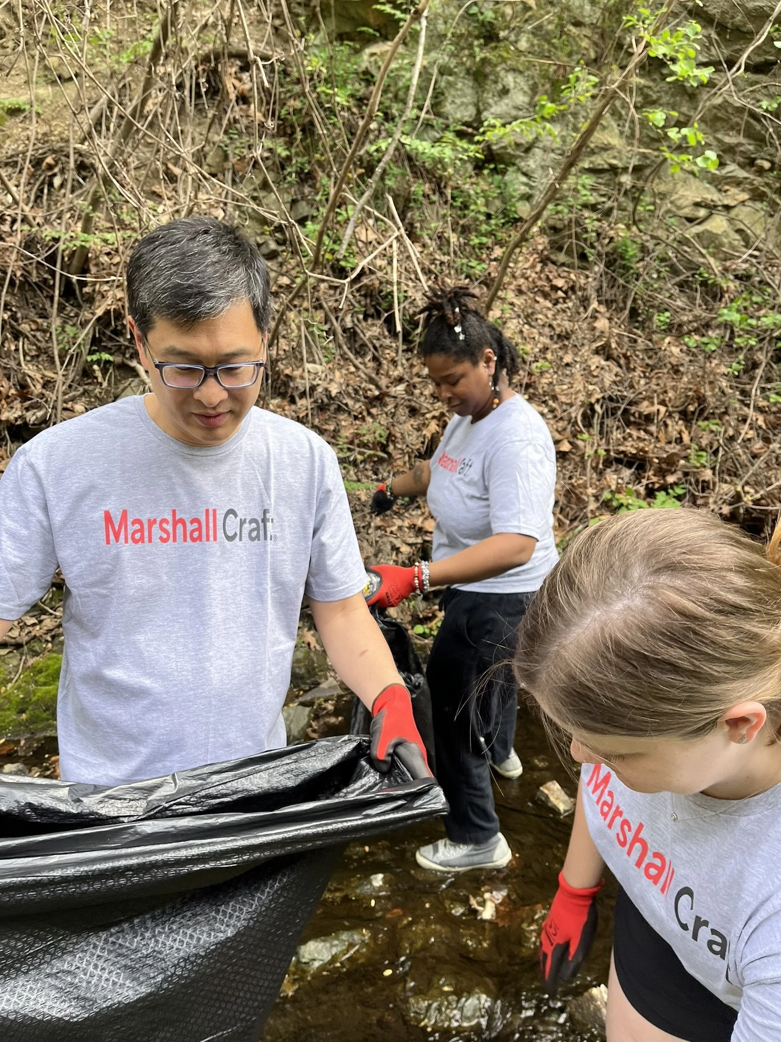 Ken, Amy, and Lilleana collect trash in the Jones Falls stream that surrounds the Baltimore office in Clipper Mill.