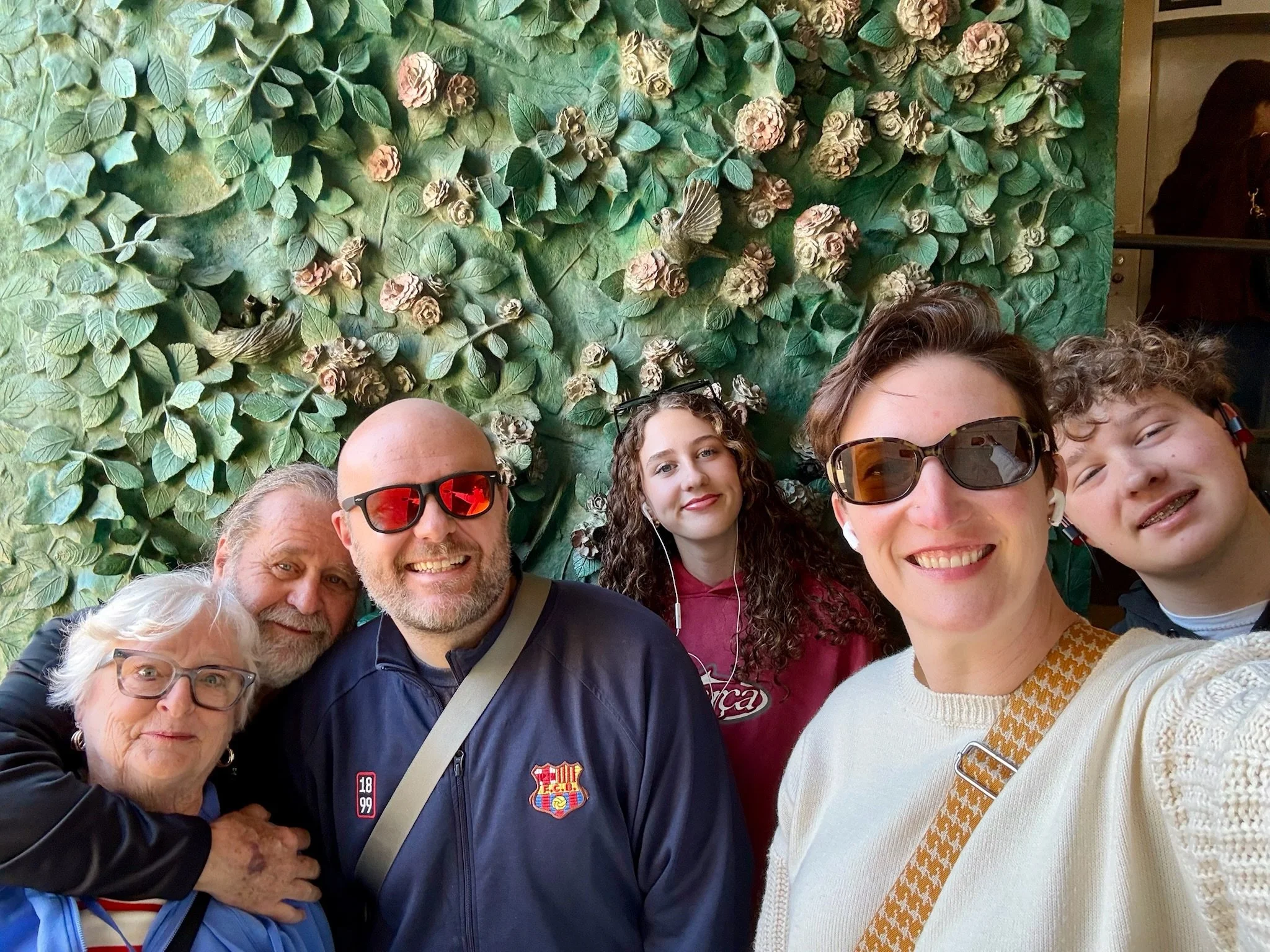 Multigenerational family group selfie in front of green sculptural leaf-and-flower relief wall