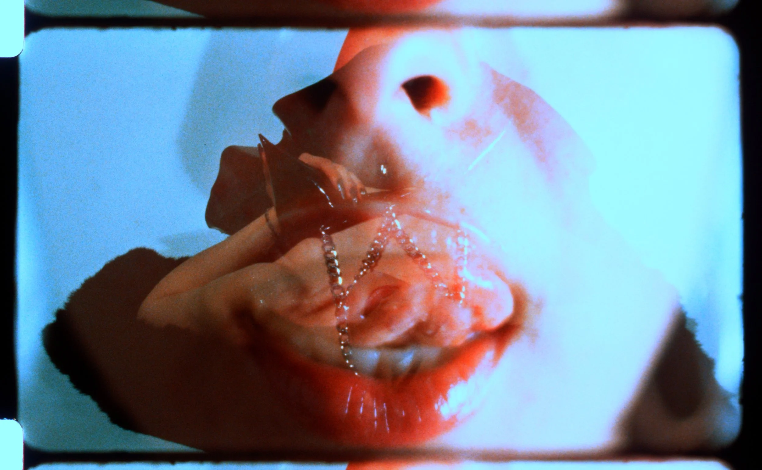 Close-up 16mm frame of lips and fingers in red and pale blue. Still from Intrusive Thots, 16mm film by Hartenjager.