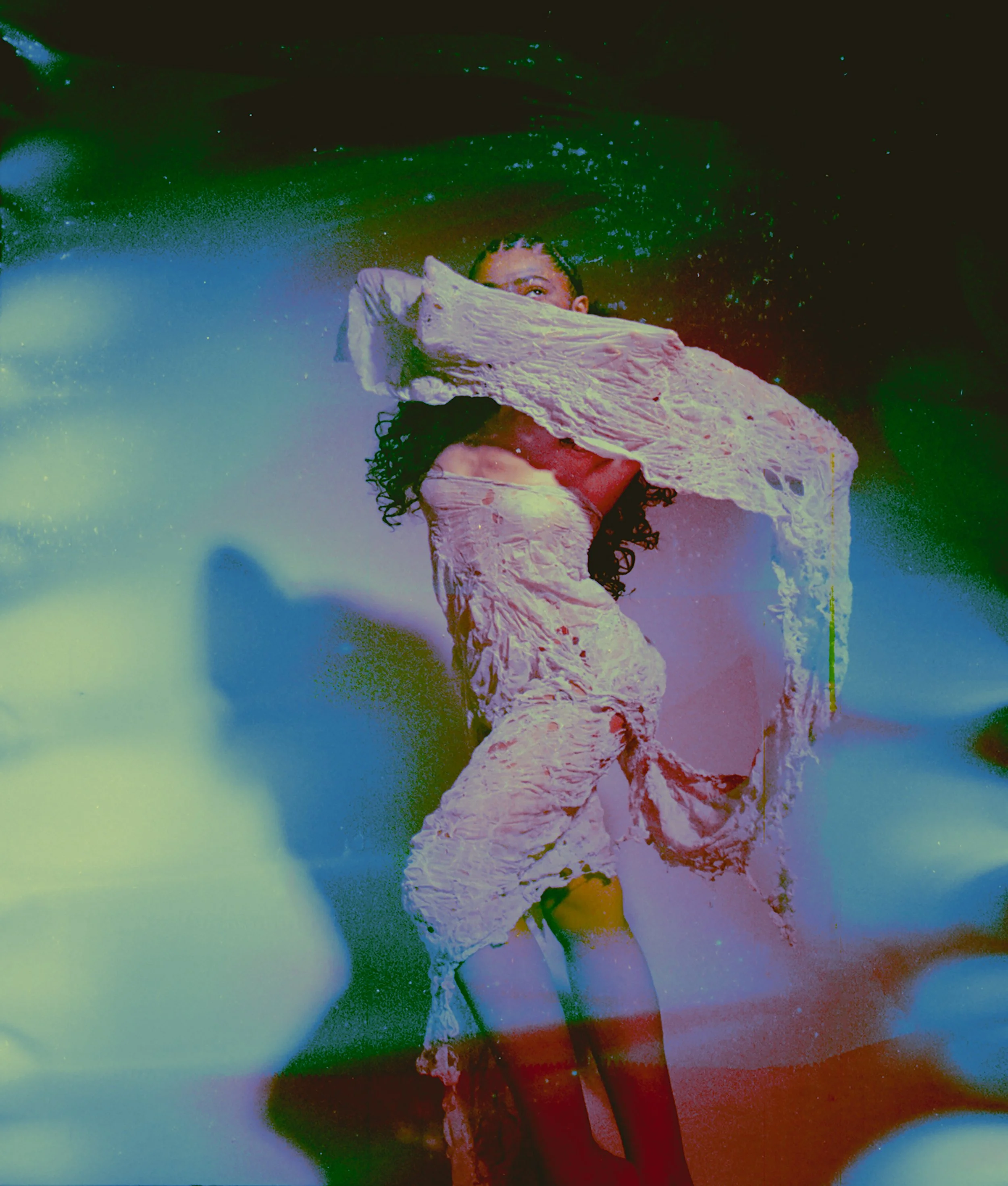 Chemically altered film image of a figure in a white garment twisting mid-movement, in green and red tones. A Moulting Tale by Hartenjager.