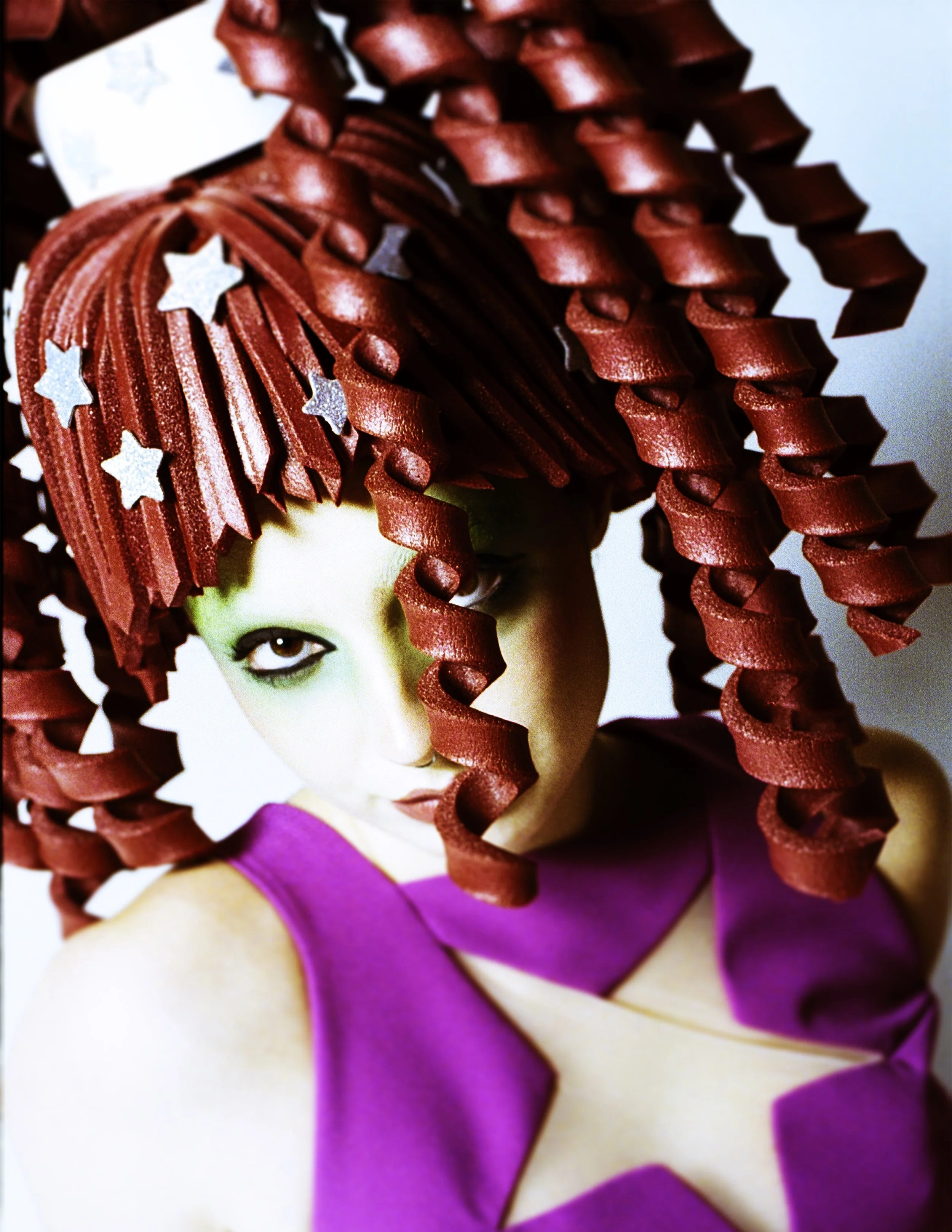 Close-up of a sculpted red corkscrew wig with star clips over a pink star-print top. Loopsyland, editorial for Kaltblut Magazine by Hartenjager.