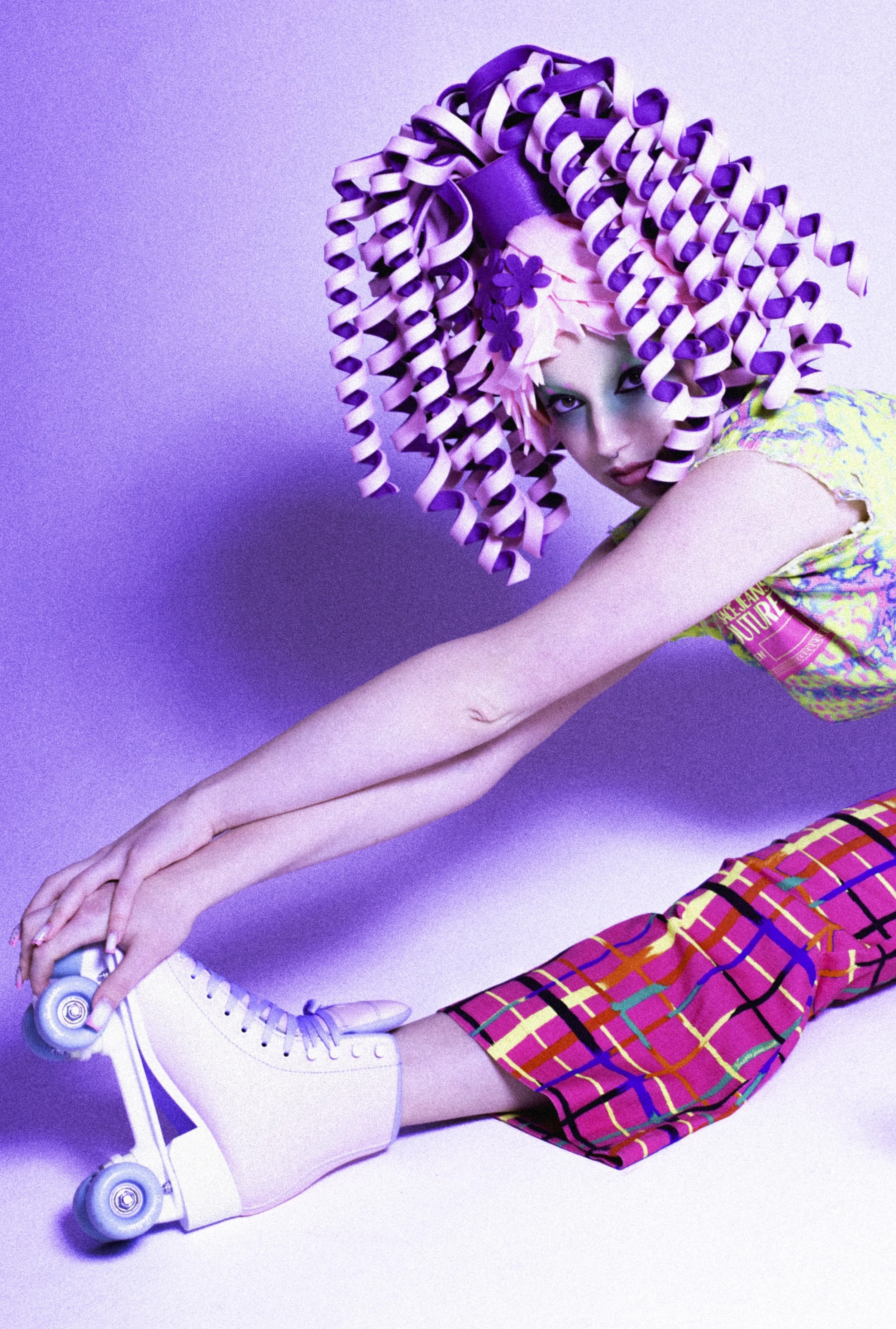 Model in a sculpted purple curl wig and pink plaid flares stretching on the floor. Loopsyland, editorial for Kaltblut Magazine by Hartenjager.