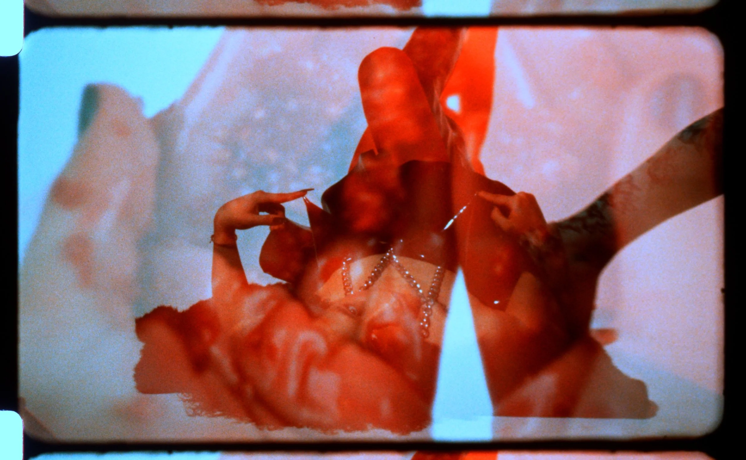Double exposed 16mm frame of hands and skin in pale blue and red. Still from Intrusive Thots, 16mm film by Hartenjager.