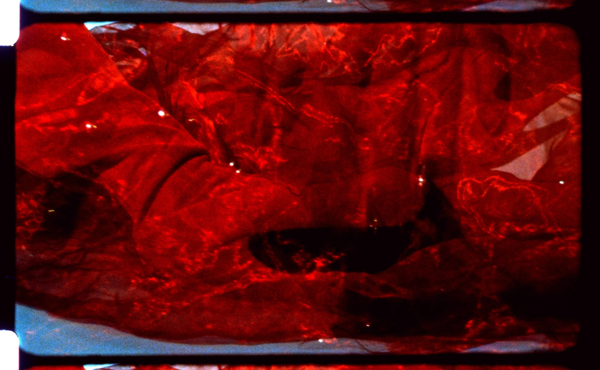 Red-tinted 16mm frame of bodies and fabric pressed close together. Still from Intrusive Thots, 16mm film by Hartenjager.