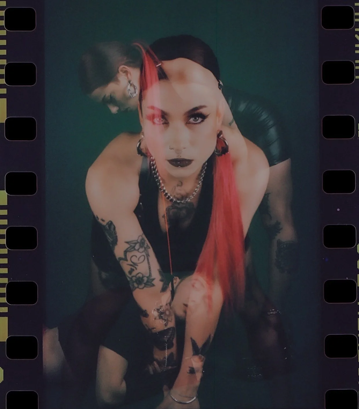 Film frame with sprocket holes: a tattooed model with red and black hair crouching, double exposed in dark green. Dominance by Hartenjager.