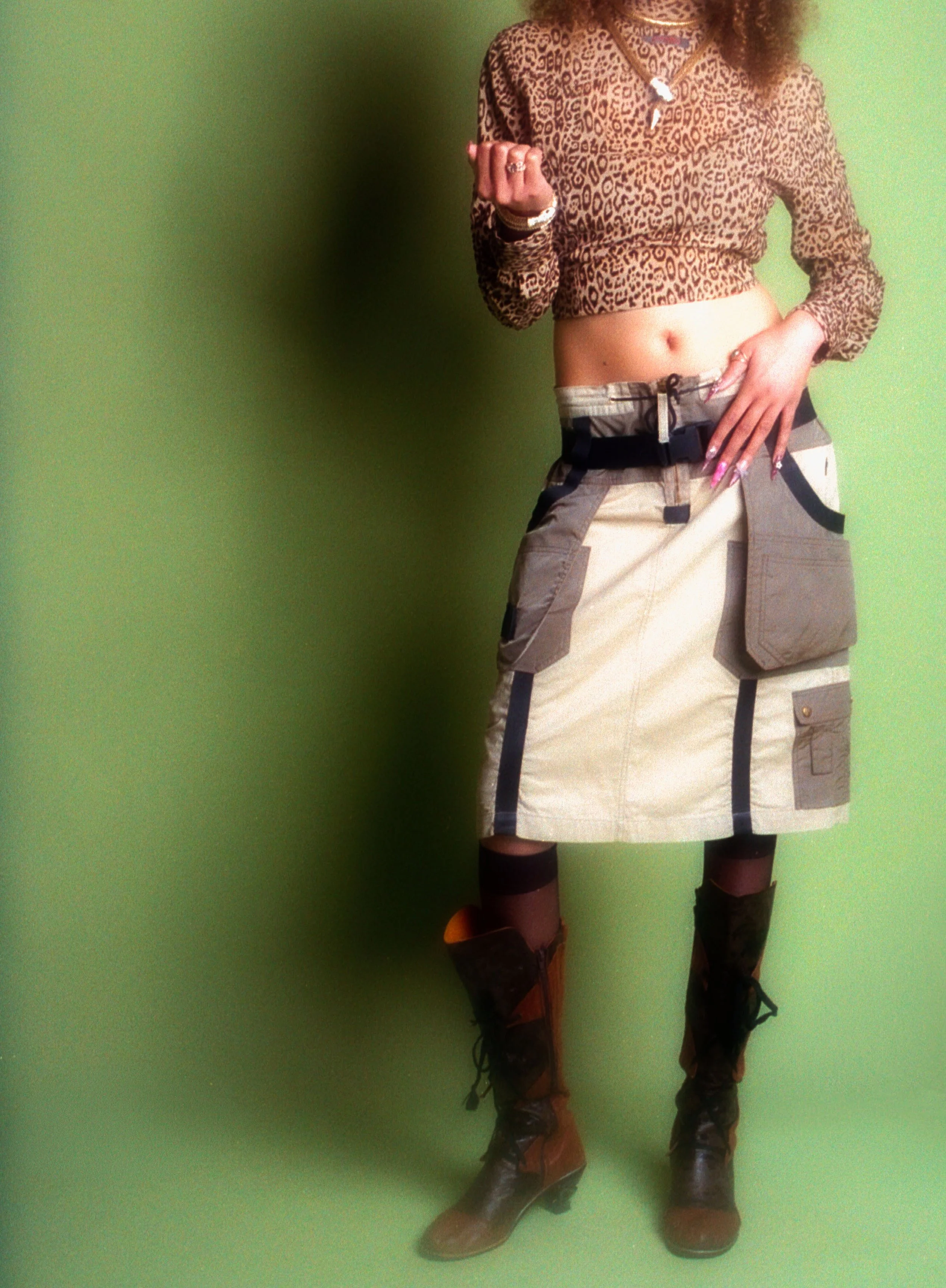 Cropped view of a leopard print top, patchwork mini skirt and knee-high boots against green. Vintáááge May by Hartenjager.