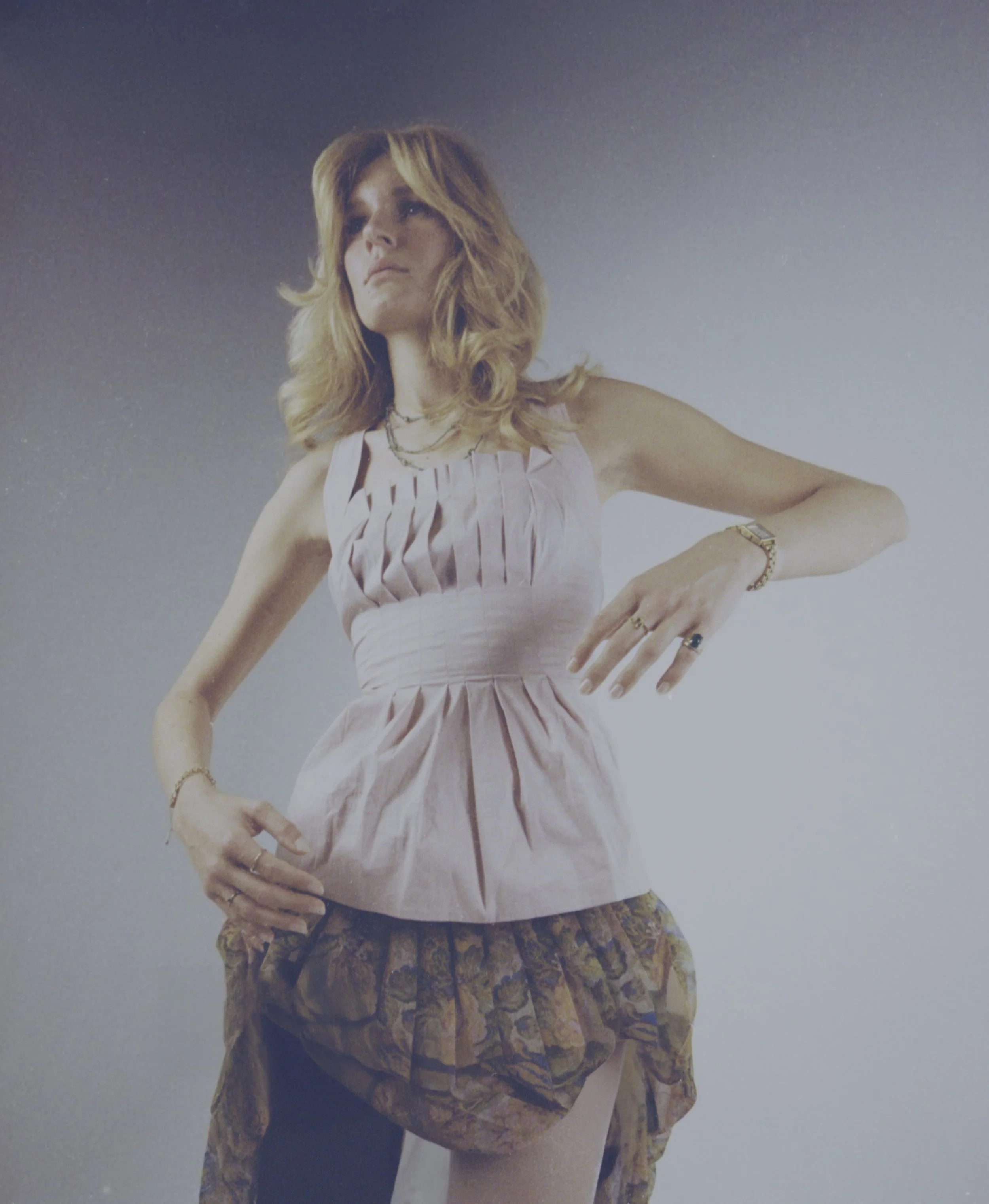 Blonde model in a ruched white top and ruffled brown skirt against a grey backdrop. Vintáááge January by Hartenjager.