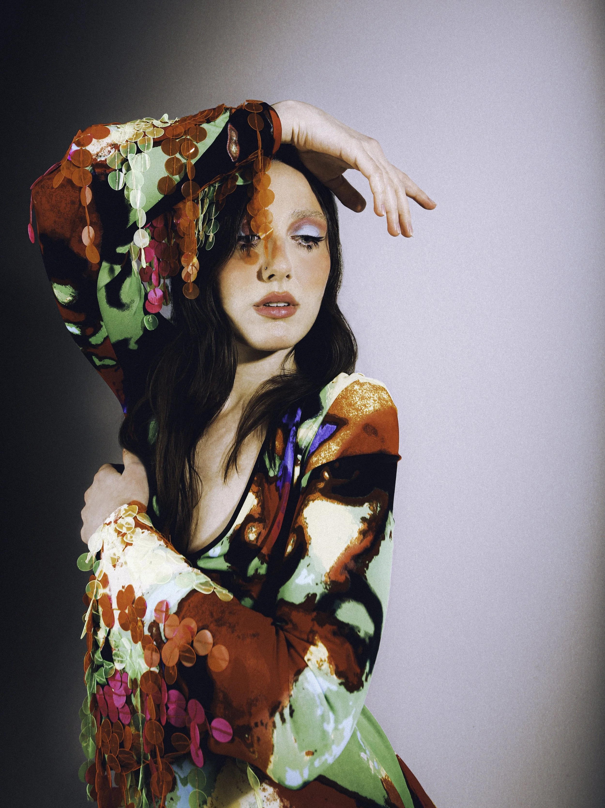 Dark-haired model in a red and green floral printed jacket, one arm raised over her head. Vintáááge March by Hartenjager.
