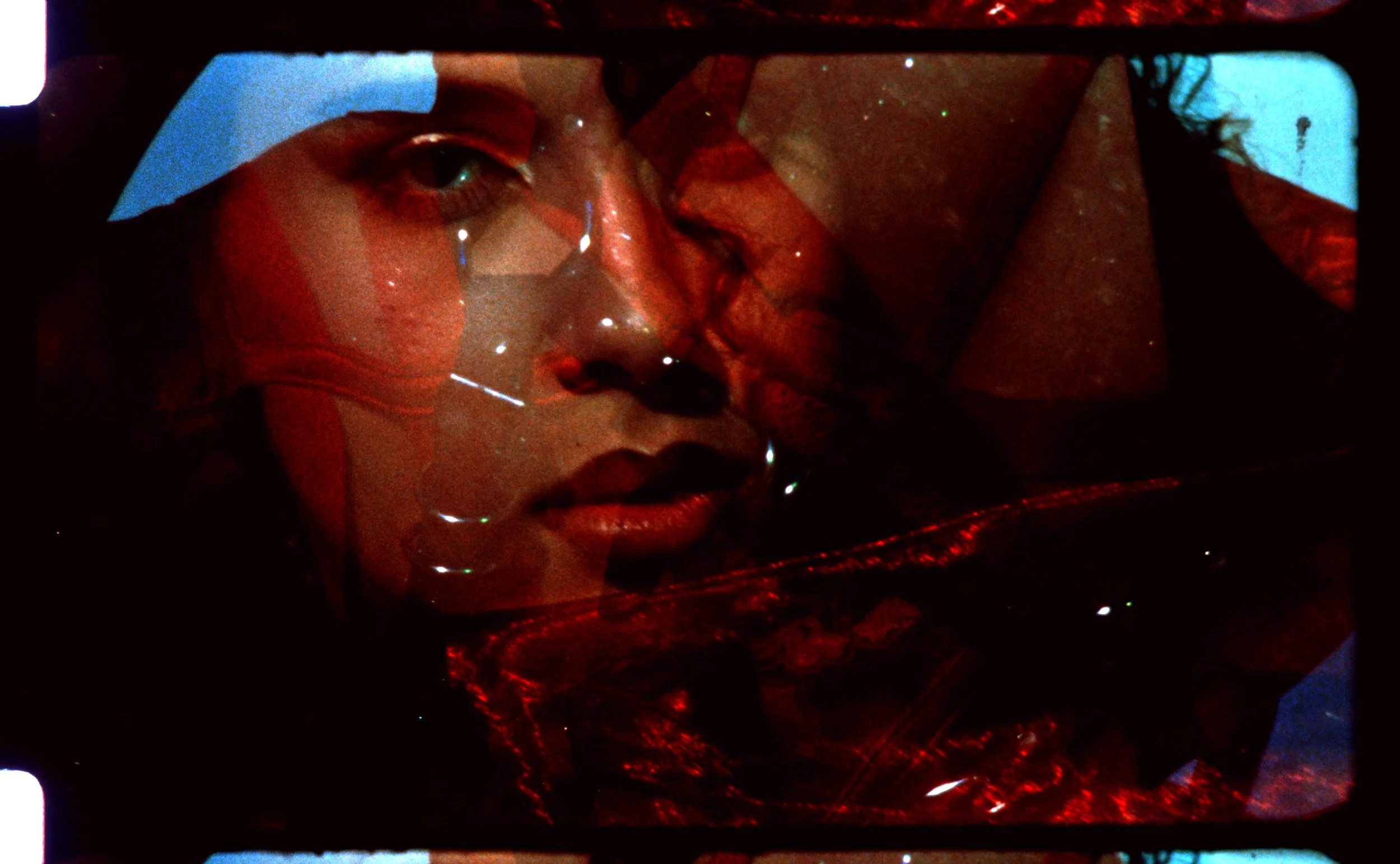 Close-up 16mm frame of a face in warm red tones, overlaid with a second exposure. Still from Intrusive Thots, 16mm film by Hartenjager.