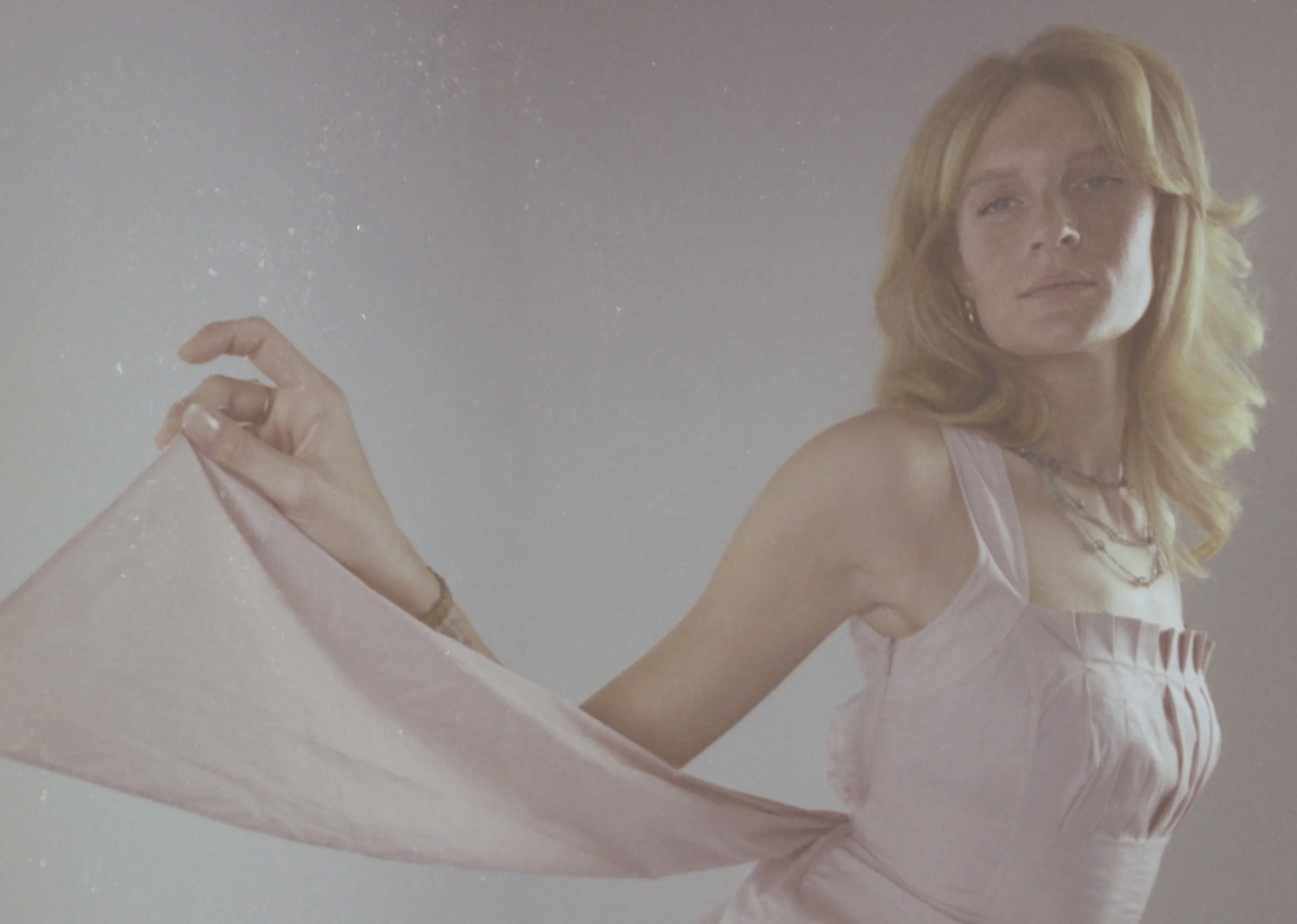 Blonde model in a pale pink slip dress letting a sheer pink scarf drift from her hand. Vintáááge January by Hartenjager.