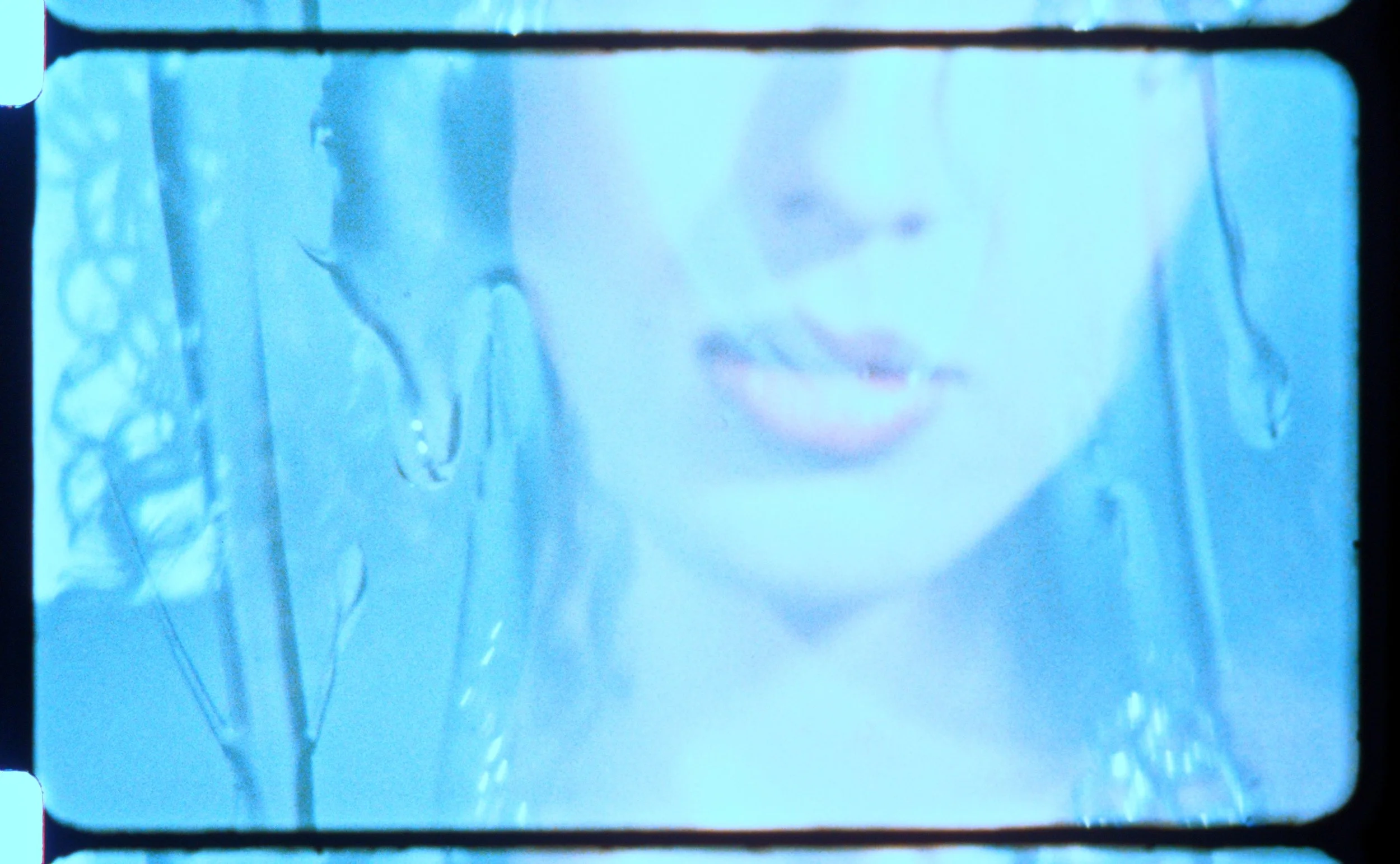 Pale blue 16mm frame of a face with parted lips, softly overexposed. Still from Intrusive Thots, 16mm film by Hartenjager.
