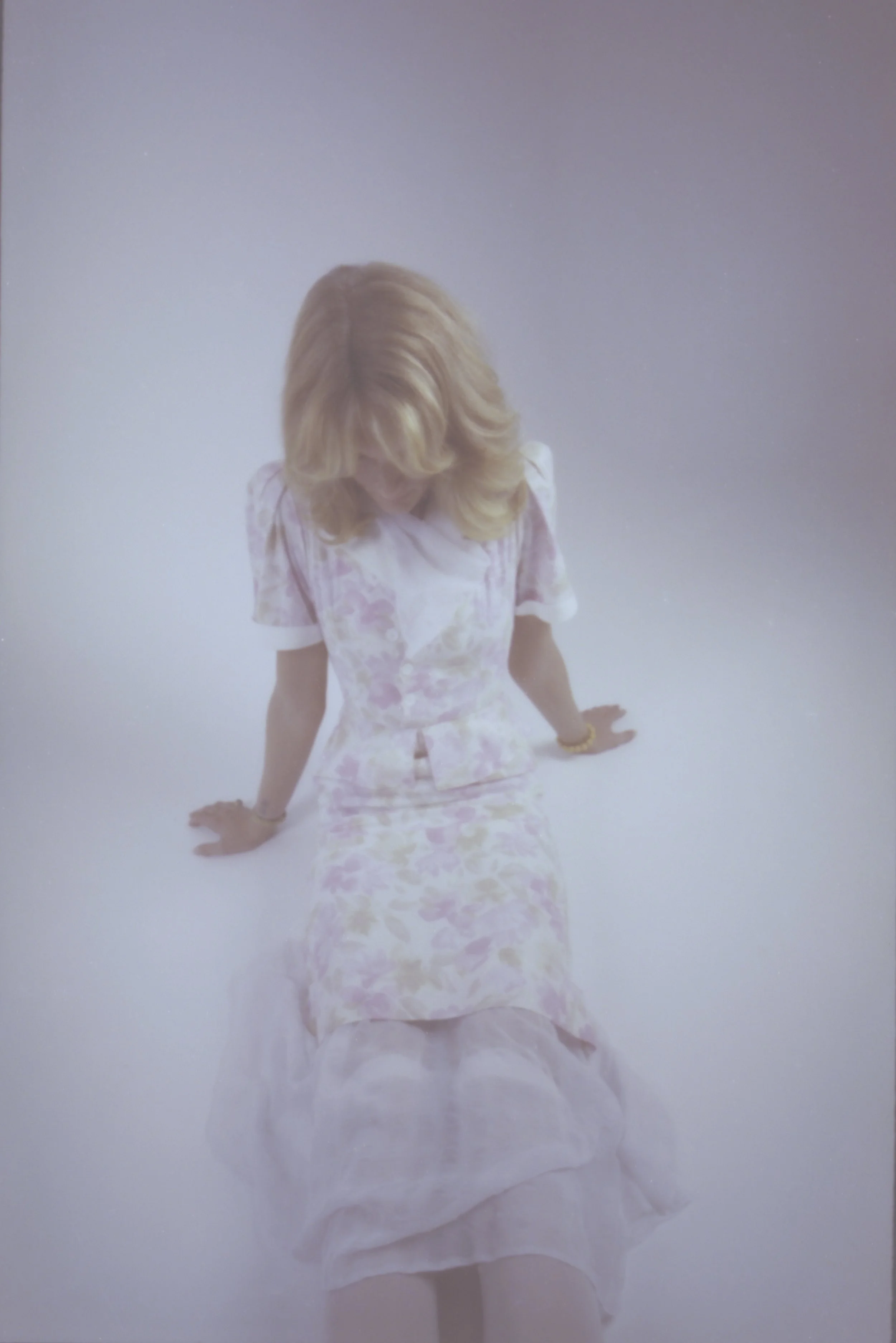 Blonde model in a white lace dress, softly blurred against a pale backdrop. Vintáááge January by Hartenjager.