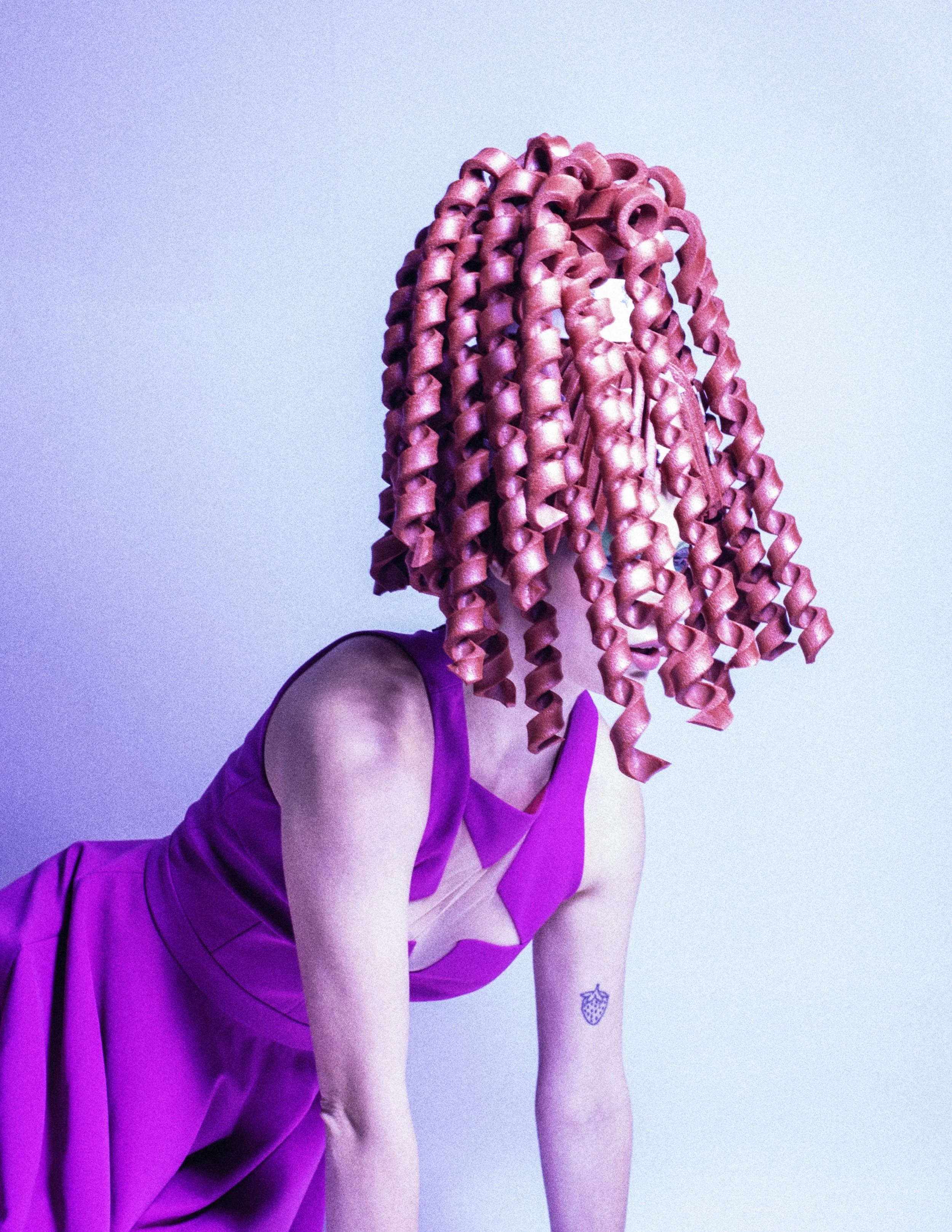 Model in a pink top bending forward, face hidden by a sculpted pink corkscrew-curl wig. Loopsyland, editorial for Kaltblut Magazine by Hartenjager.