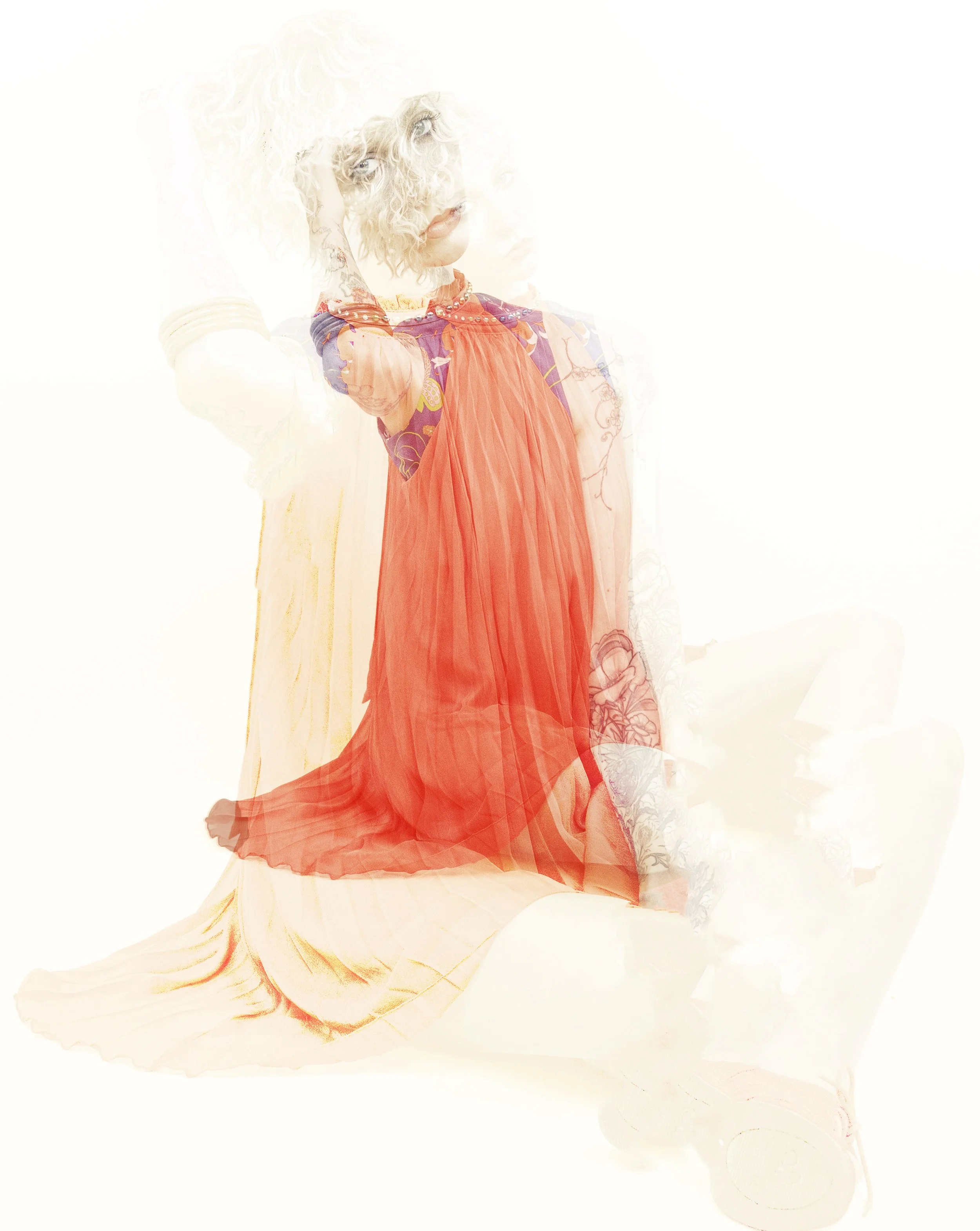 Overexposed film portrait of a blonde person in a red dress, sitting with knees drawn up. By Hartenjager.