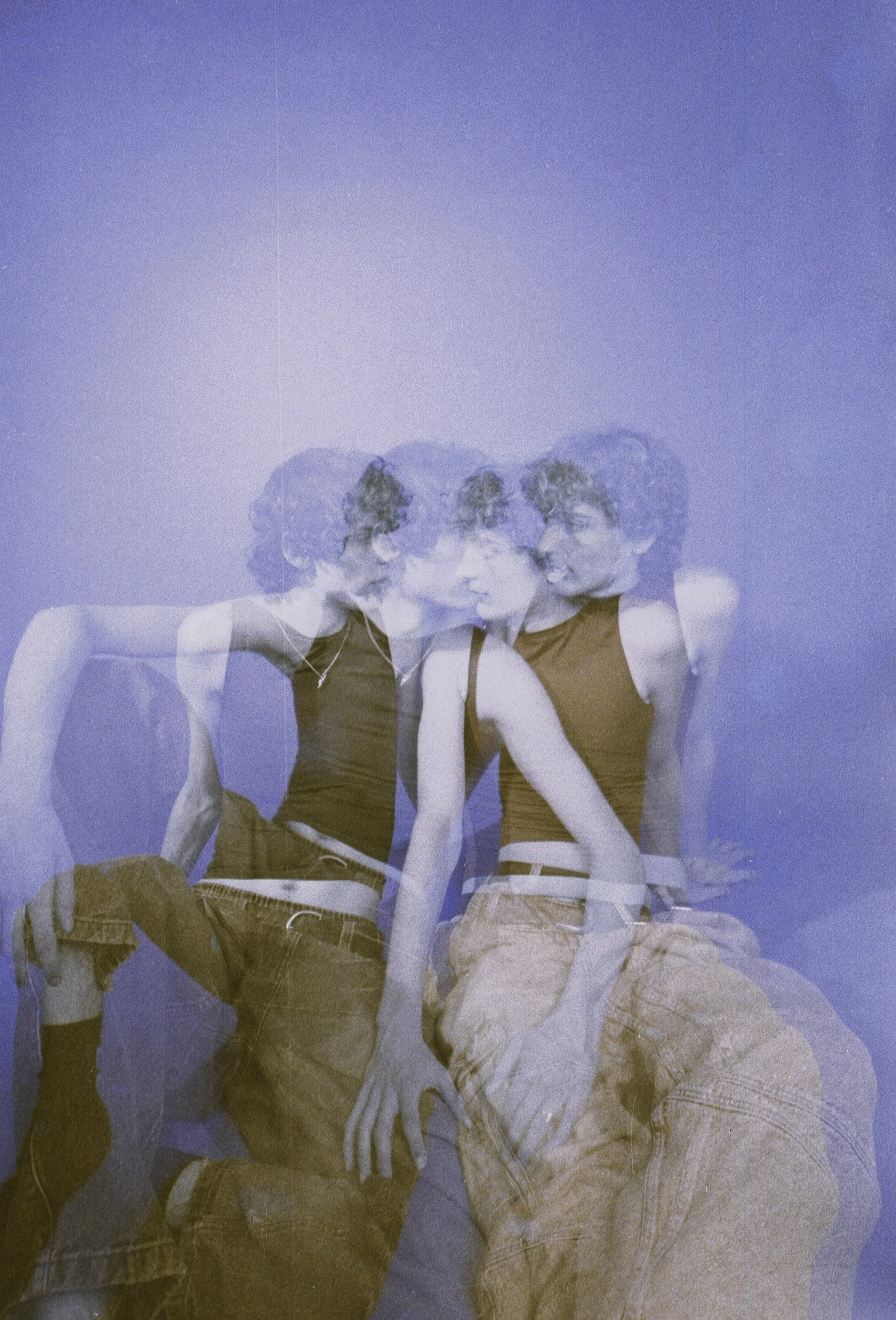 Two men in vests sitting entangled, multiplied by layered exposures against a blue backdrop. Geminus by Hartenjager.