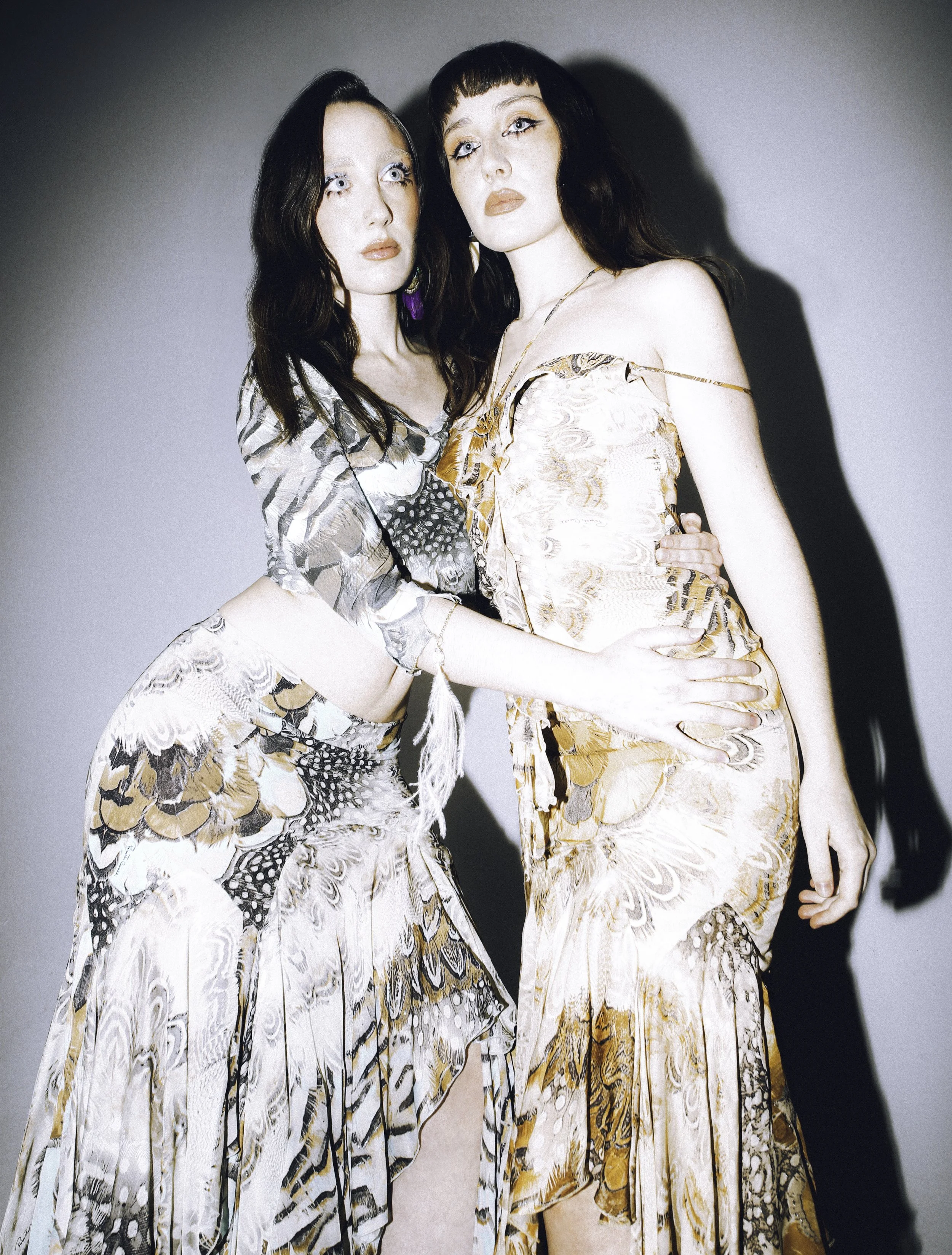 Two dark-haired models in animal-print and paisley slip dresses leaning into each other. Vintáááge March by Hartenjager.
