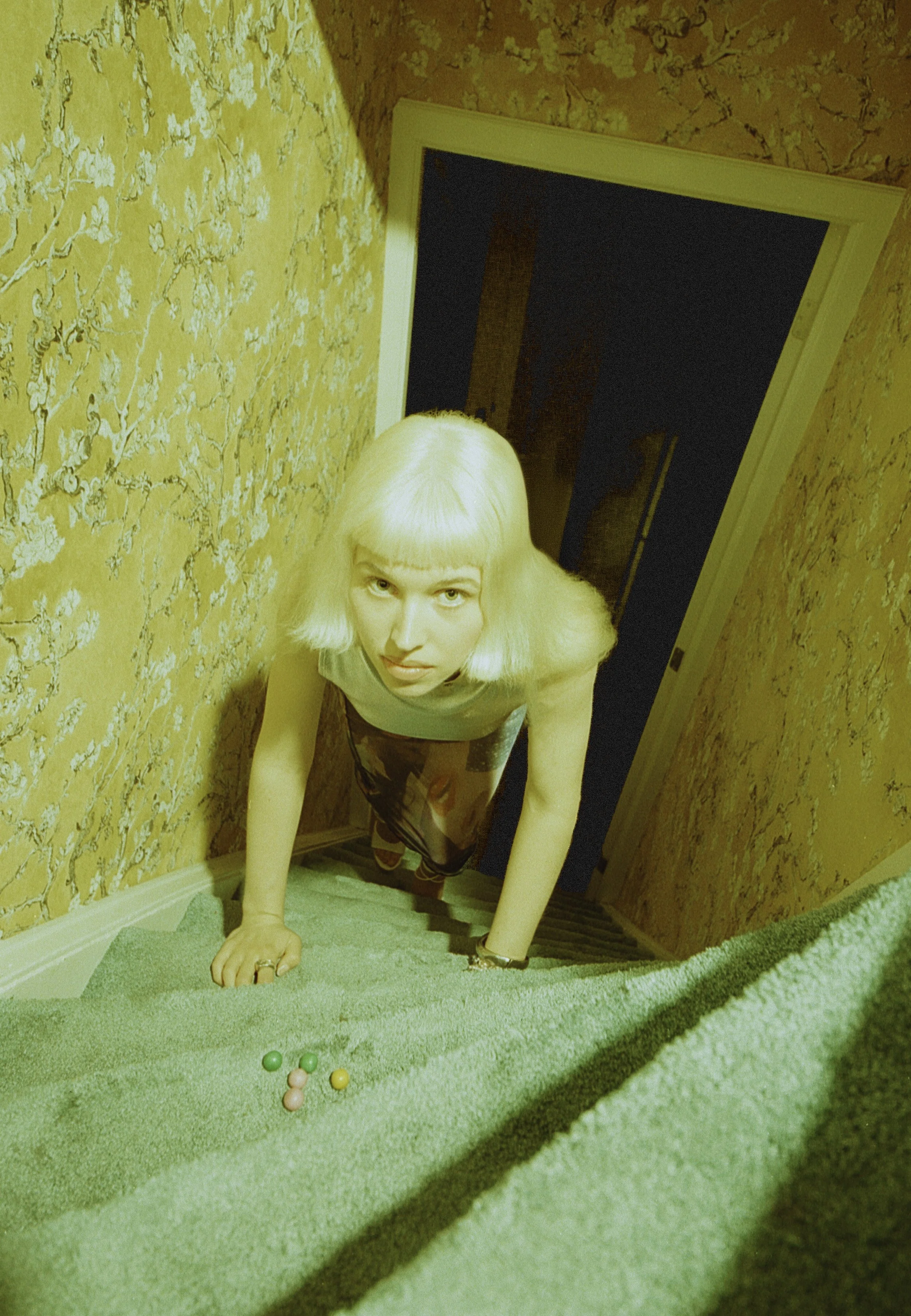 Blonde model in silver crawling up a narrow staircase toward a dark doorway. Bubblehead by Hartenjager.
