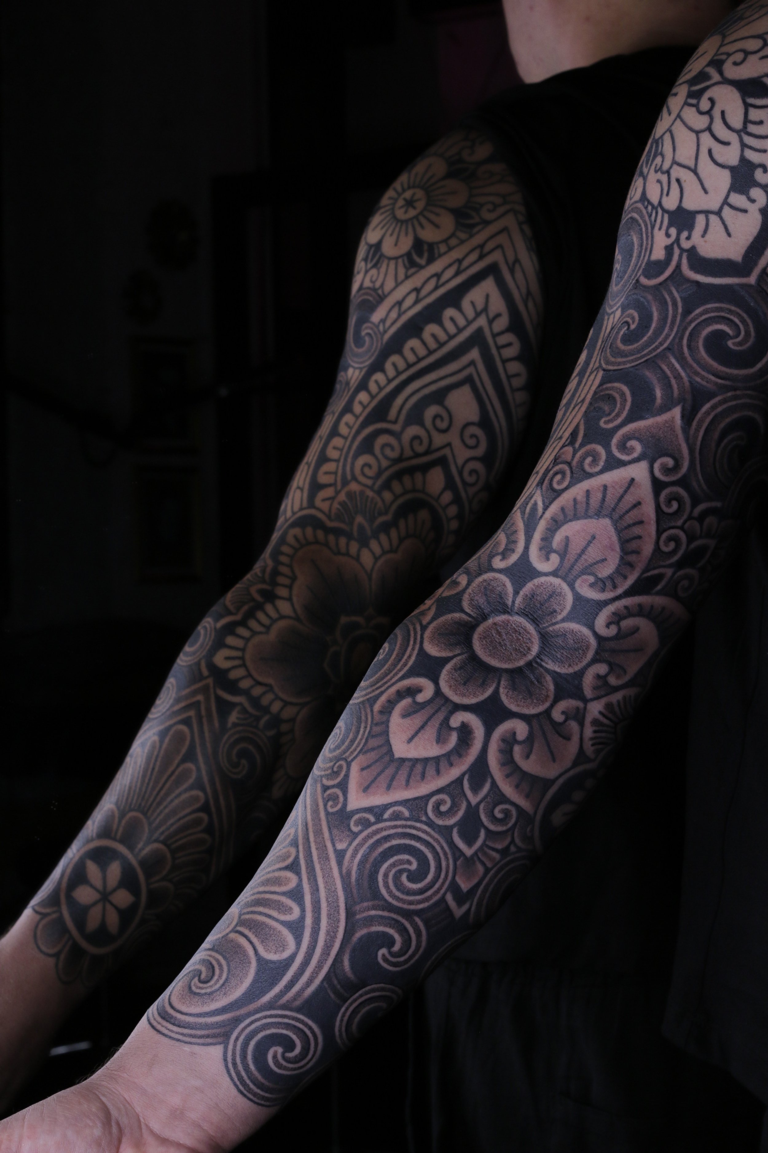 Close-up of person with extensive blackwork tattoo sleeve on arm, featuring flowers, swirls, and geometric patterns. In Balinese style.