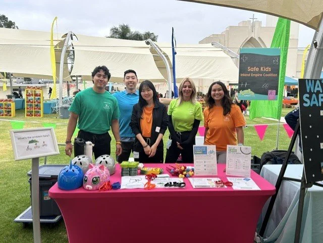 5 adults in colorful t-shirts standing behind a table of educational materials outside