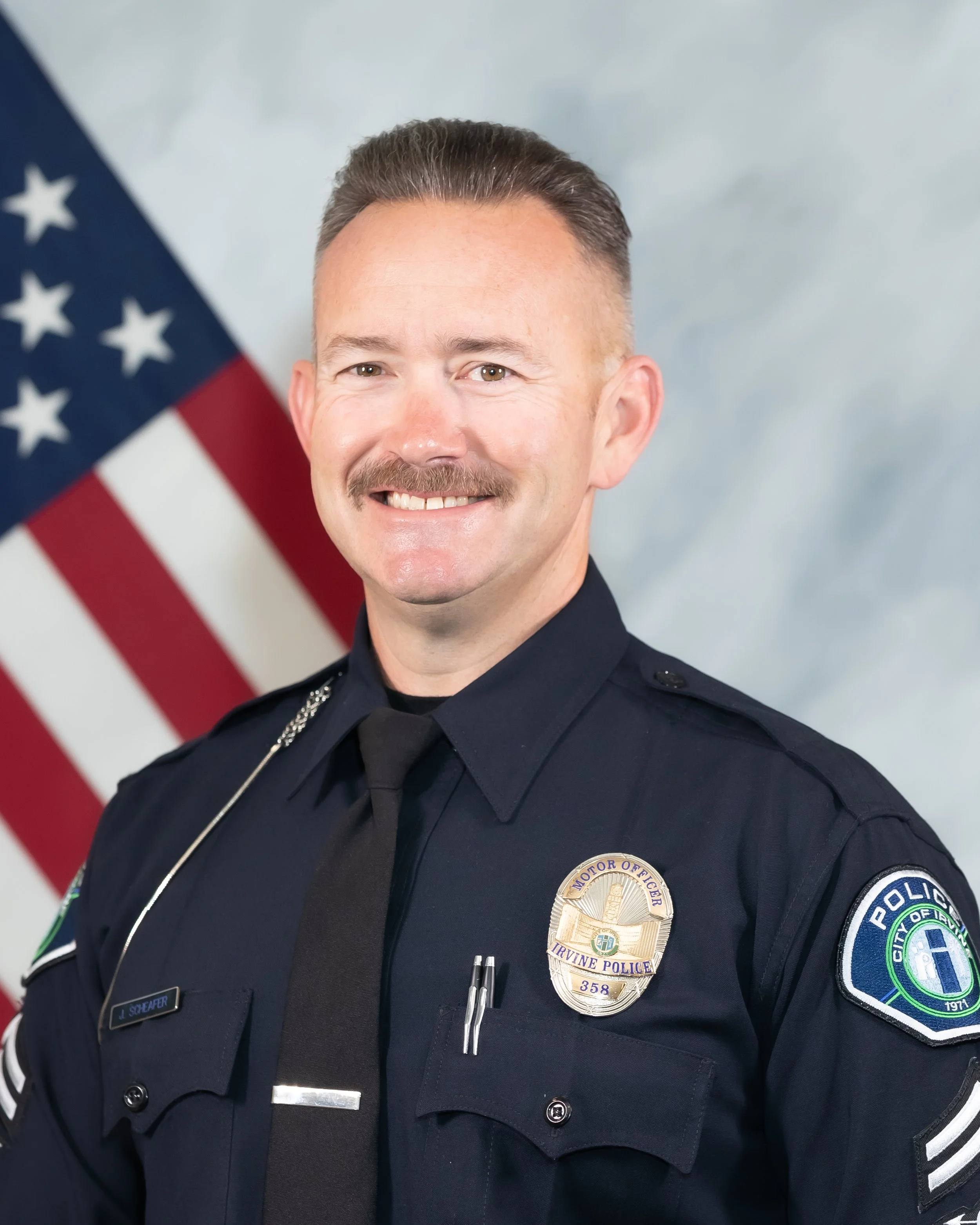 portrait of Ofc. Jason Schaefer, in police uniform, in front of an American flag