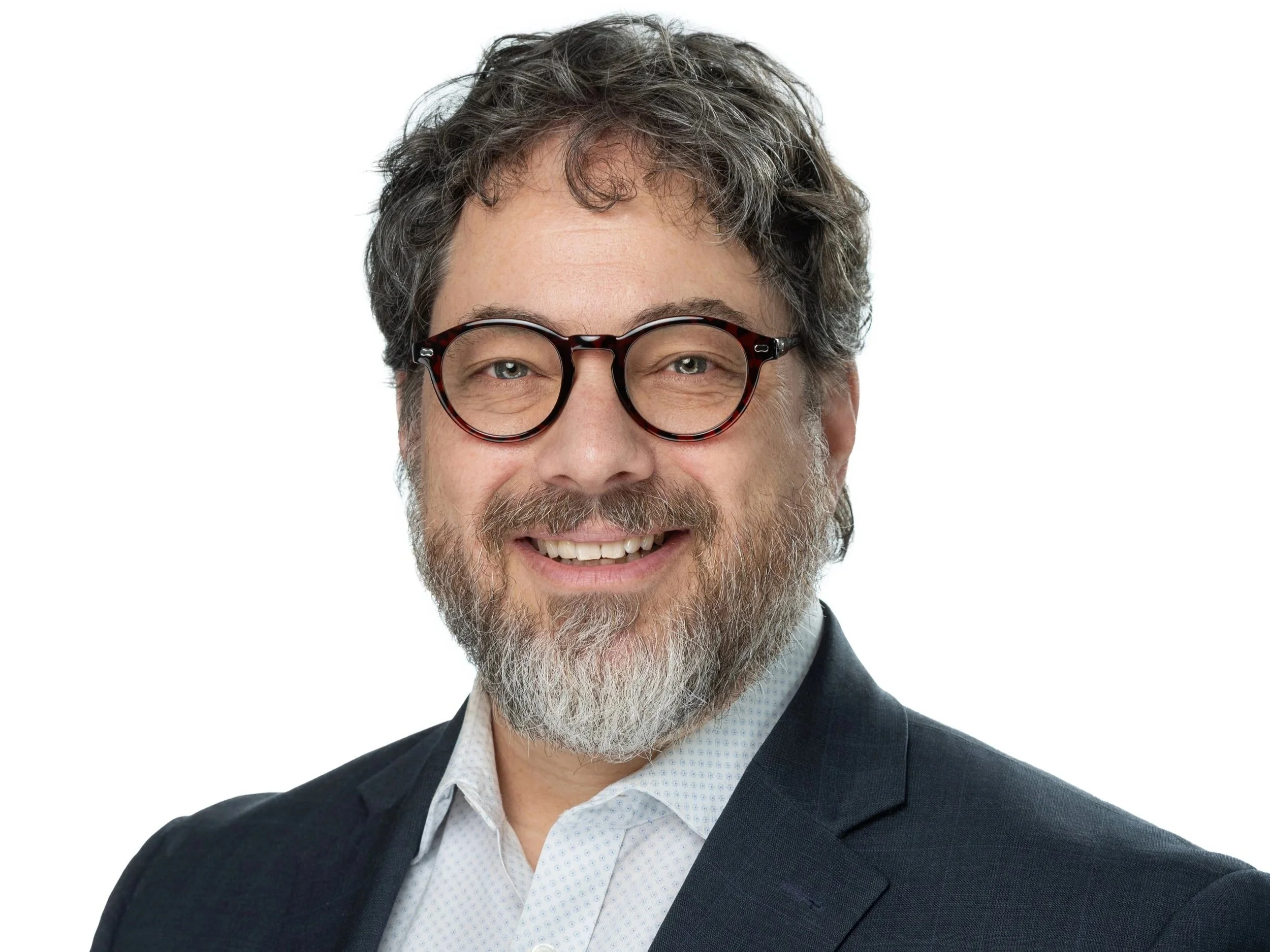 Close-up of a smiling middle-aged man with gray curly hair, a beard, glasses, wearing a dark suit and white shirt, on a white background.