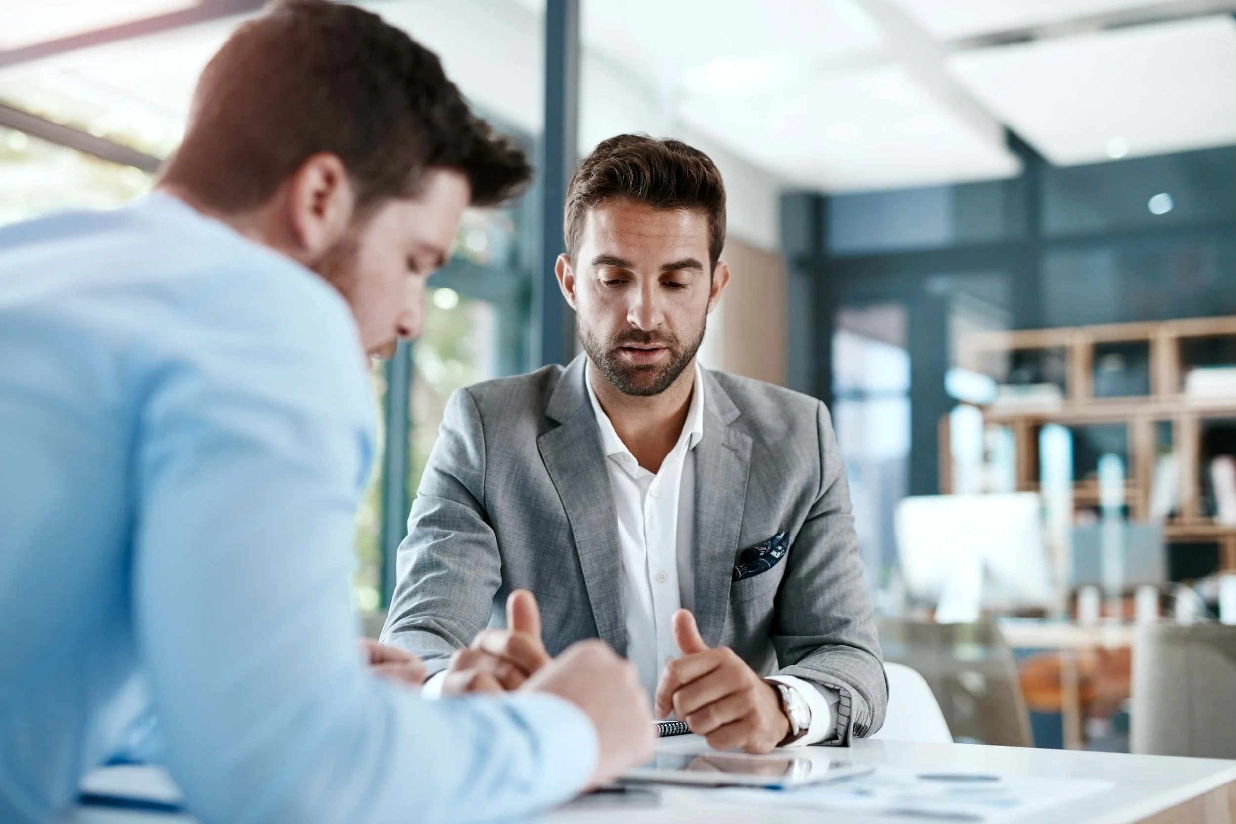 Two men in business attire having a discussion at a table in a modern office.