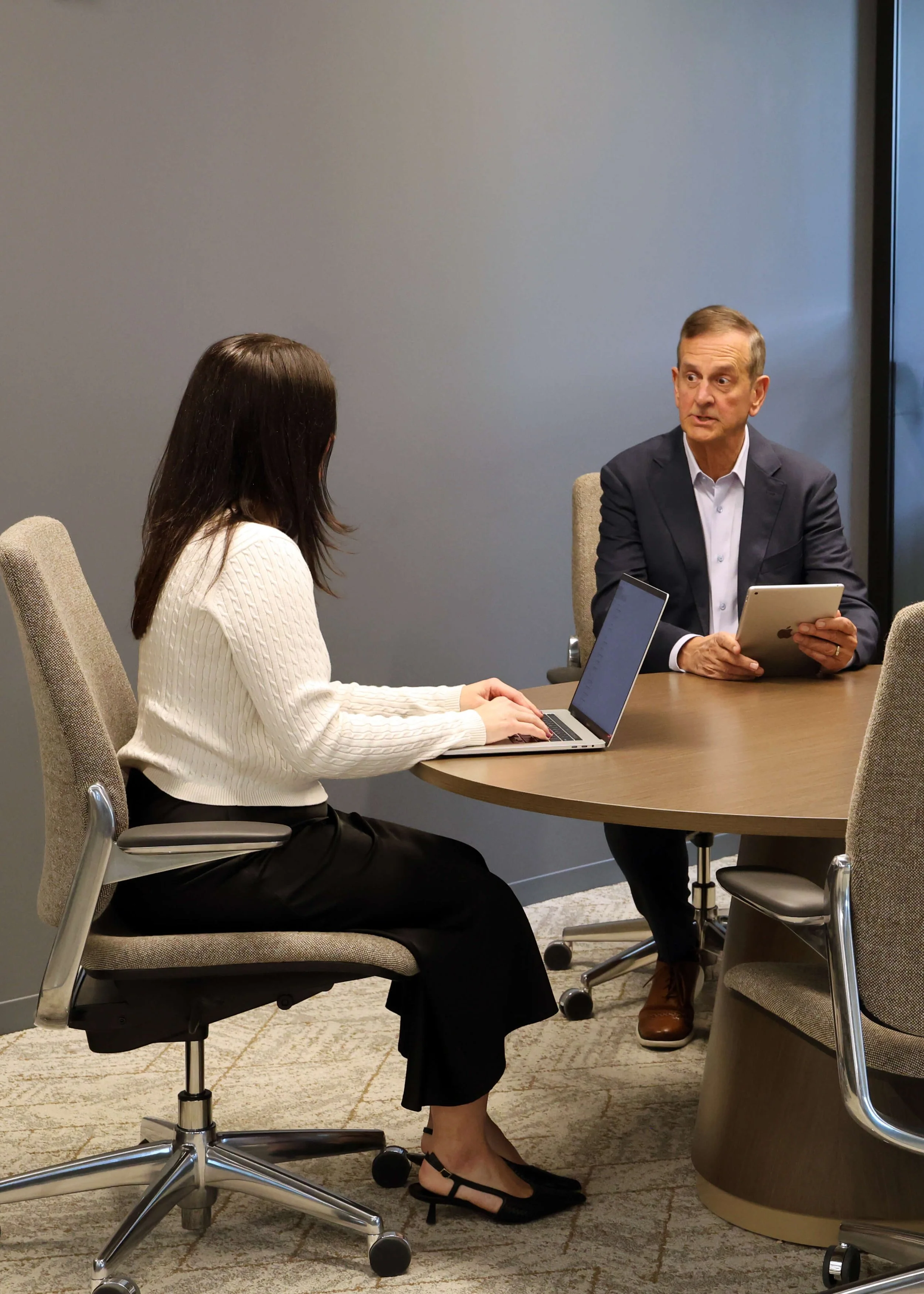 Two people having a business meeting in a conference room, a woman using a laptop and a man holding a tablet.