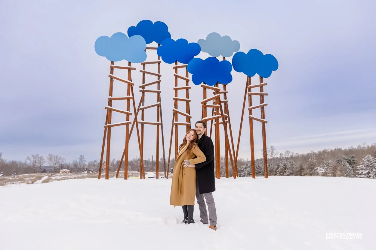 Engaged couple standing in the snow beneath outdoor sculptures at Art Omi in Ghent, New York