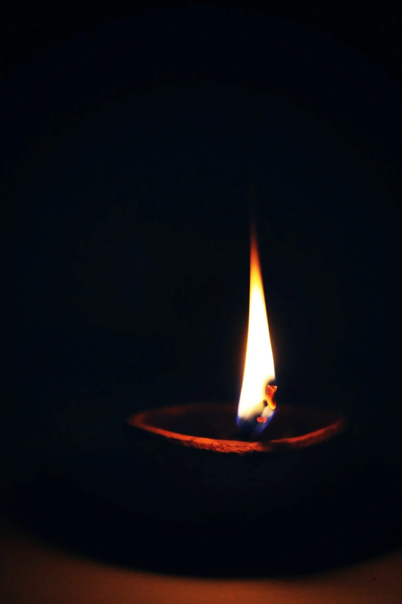 Close-up of a single lit candle flame against a dark background.